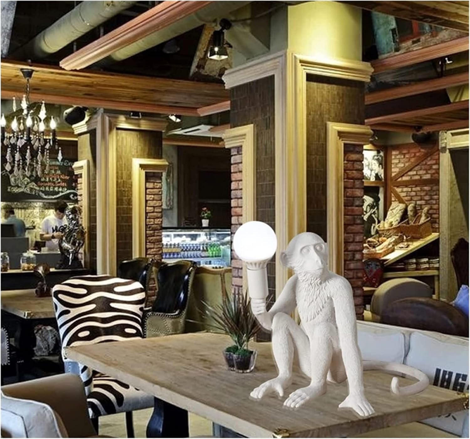 Una estatua de mono blanco sosteniendo una bombilla. El mono está sentado en una mesa de madera en una habitación con bar.