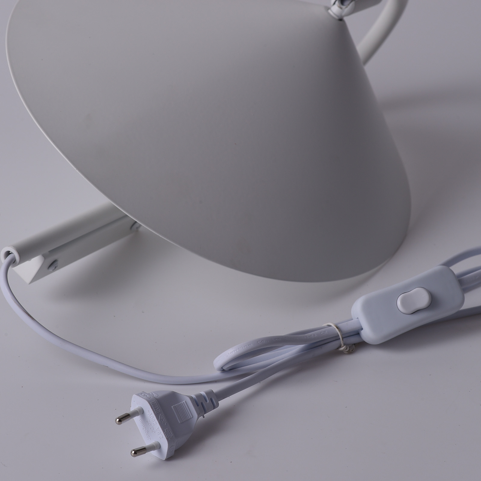 Primer plano de los componentes de una lámpara de pared. La lámpara tiene enchufe, cable, interruptor y pantalla blancos.