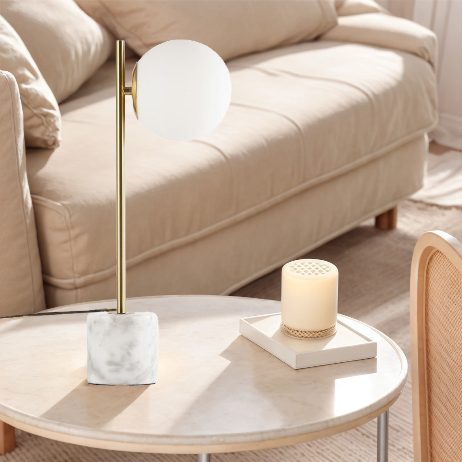 Una lámpara de mesa con pantalla globo blanca sobre un tallo dorado, sobre base de mármol, sobre una mesa.