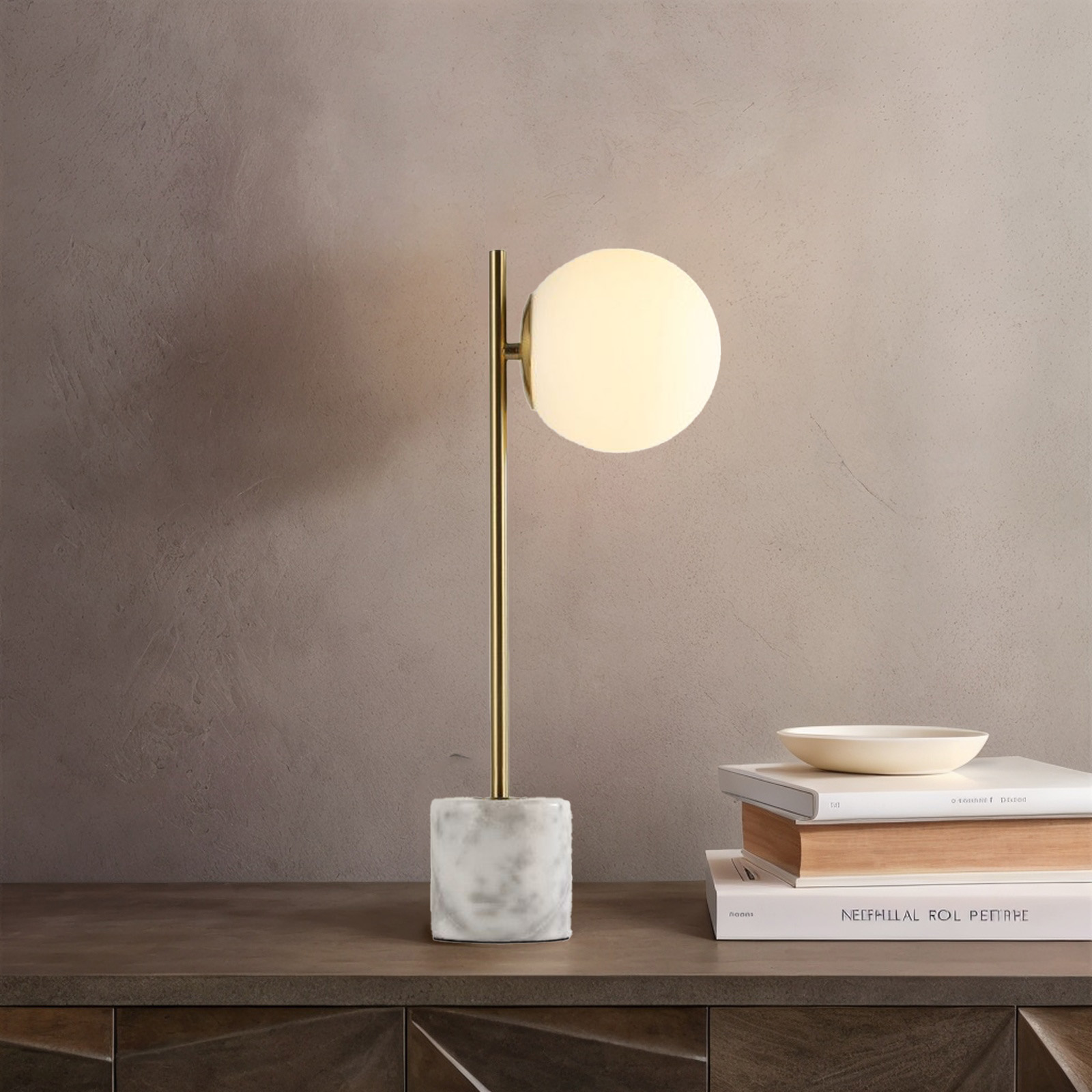 Una lámpara de mesa con pantalla globo blanca, tallo dorado y base de mármol, sobre superficie oscura.
