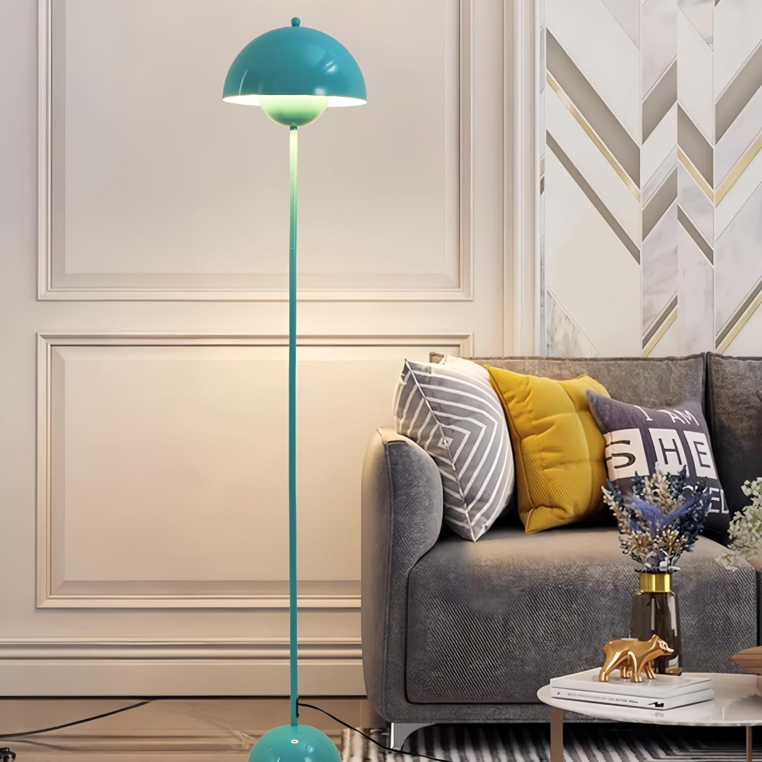Una lámpara de pie turquesa con pantalla de hongo, junto a un sofá gris y una mesa blanca.
