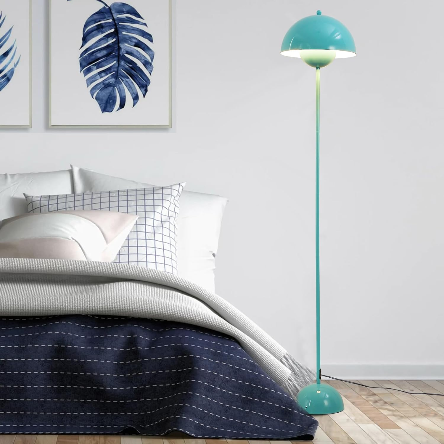Una lámpara de pie turquesa con pantalla de hongo, junto a una cama y arte mural con hojas azules.