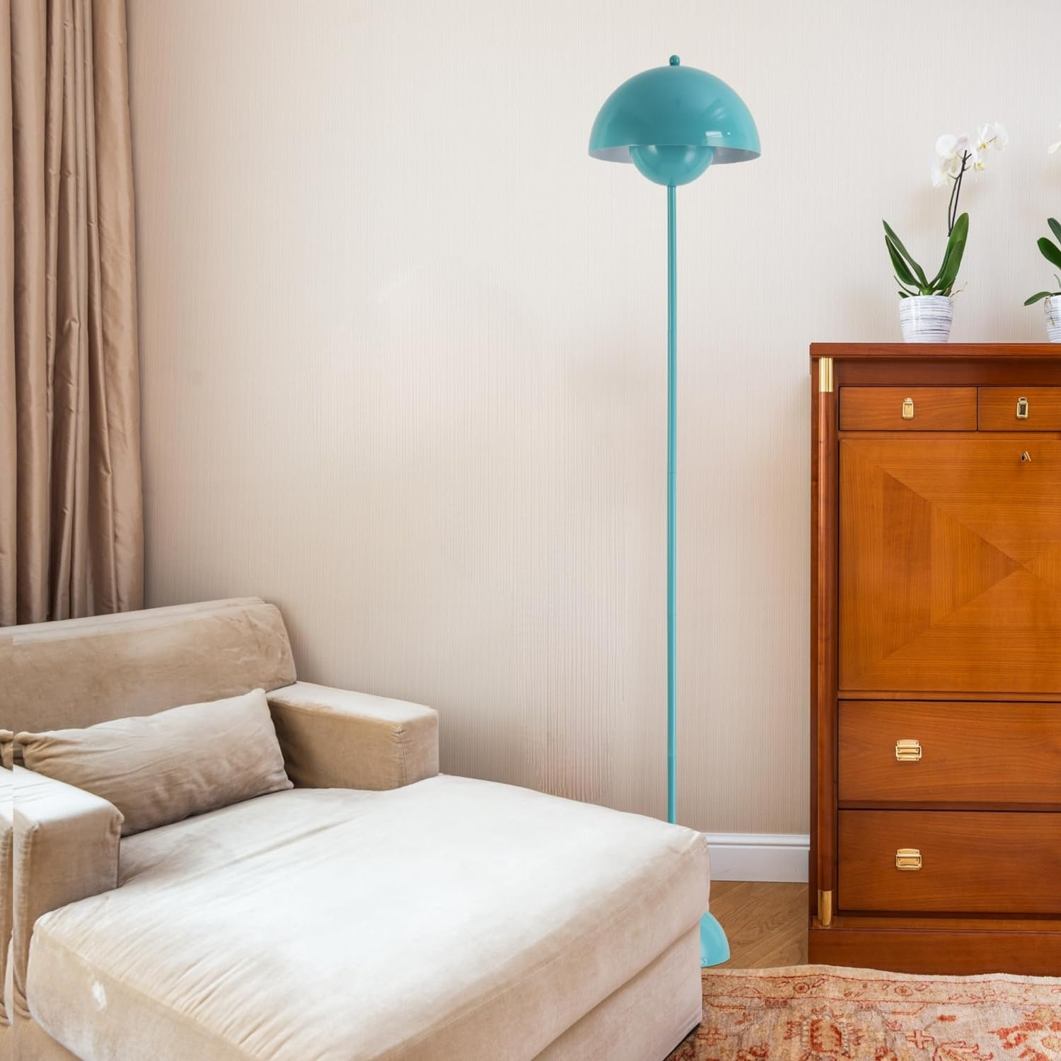 Una lámpara de pie turquesa, un chaise longue beige y un armario de madera contra una pared beige claro. Hay una alfombra en el suelo.