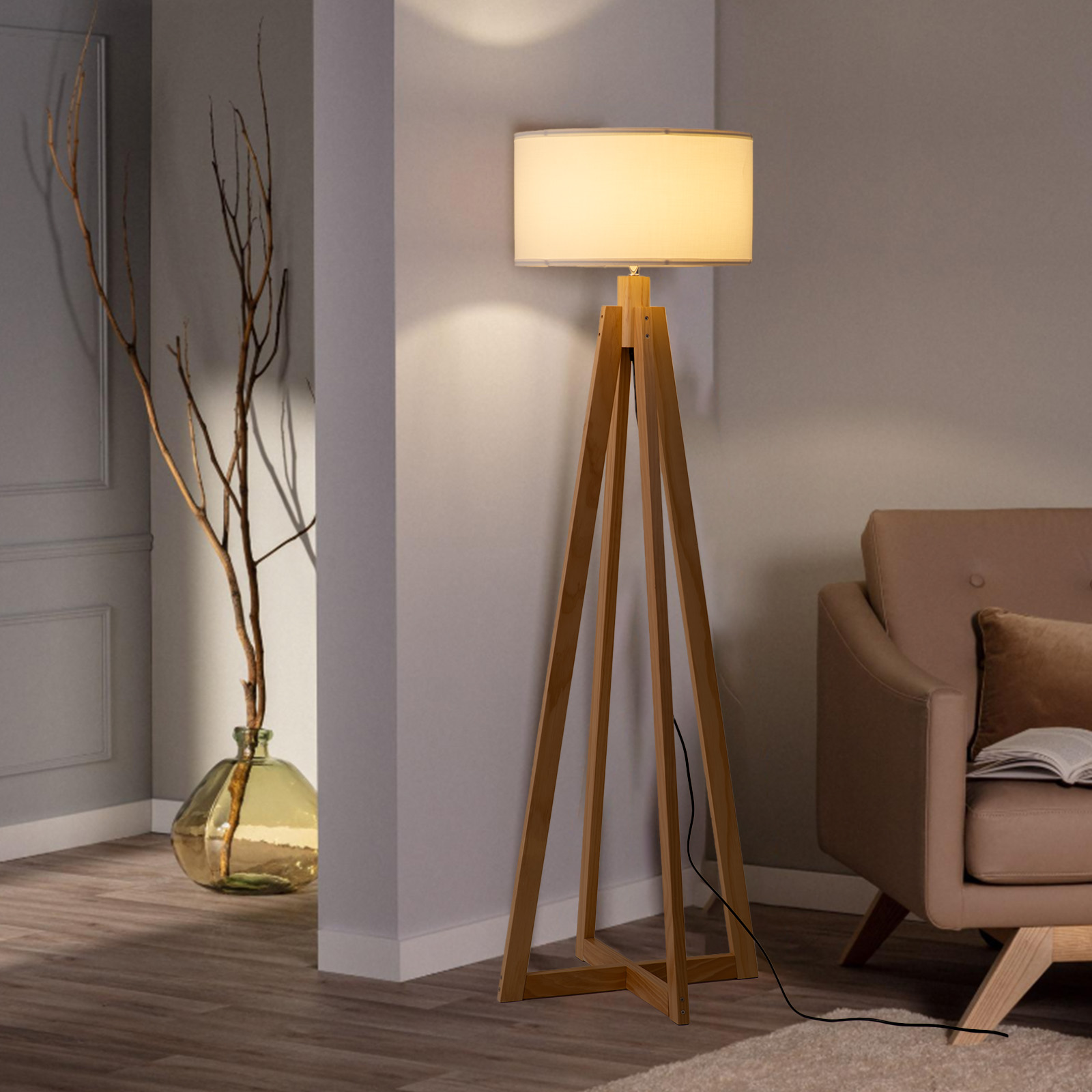 Una lámpara de pie de trípode de madera con pantalla iluminada. Jarrón con ramas.