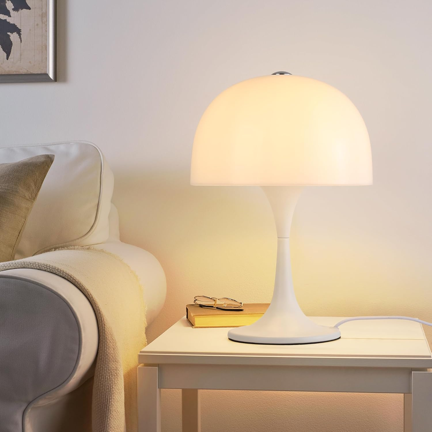 Lámpara blanca con pantalla redonda sobre una mesa. También hay un libro y gafas.