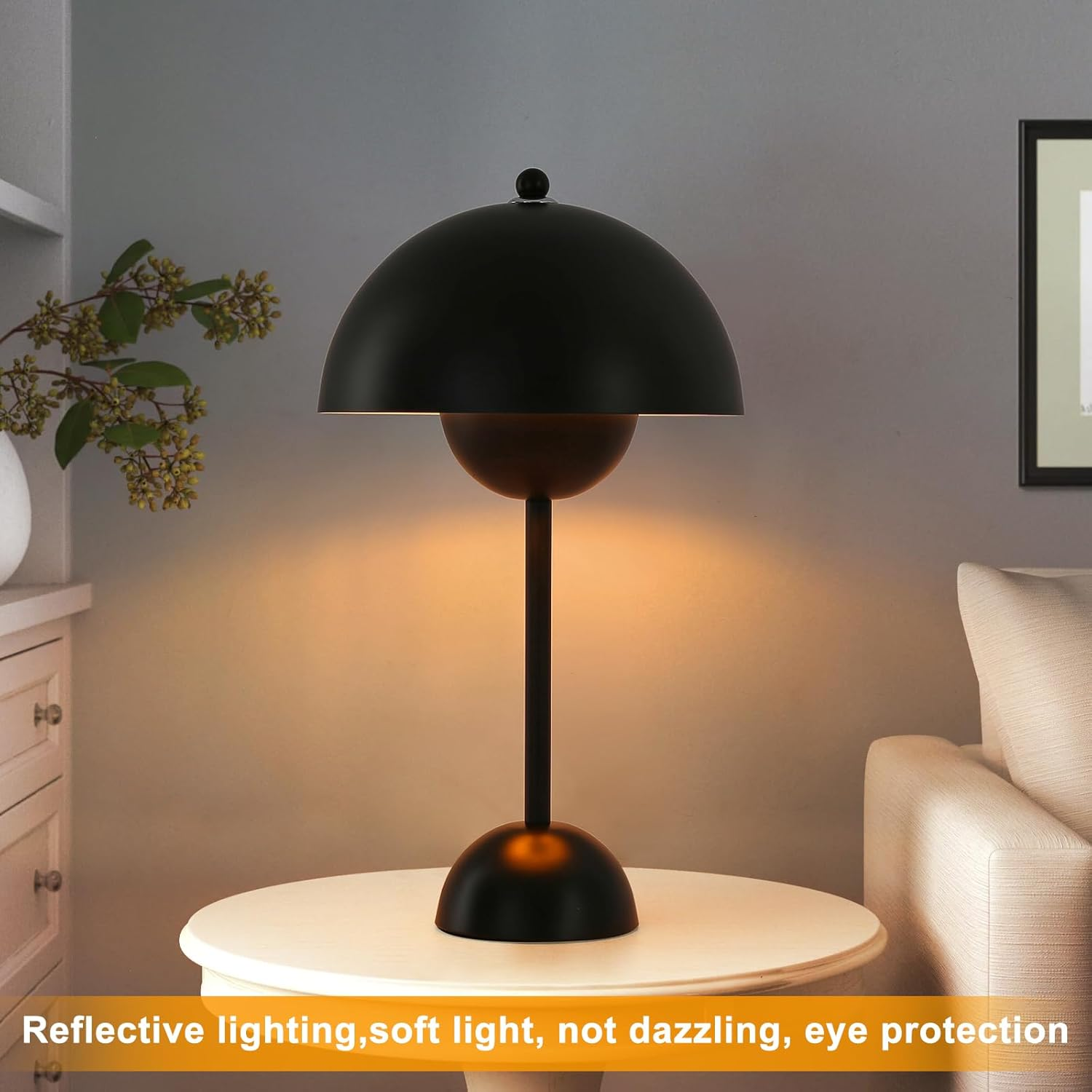 Lámpara negra sobre una mesa. Tiene pantalla y base redondeadas. La luz está encendida.