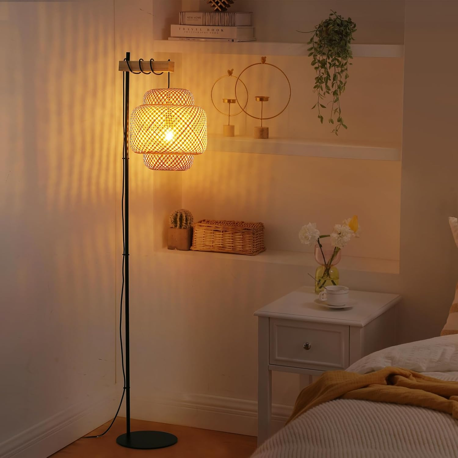 Una lámpara de pie con pantalla tejida en una habitación. Una mesita de noche, un cactus y un artículo decorativo son visibles.