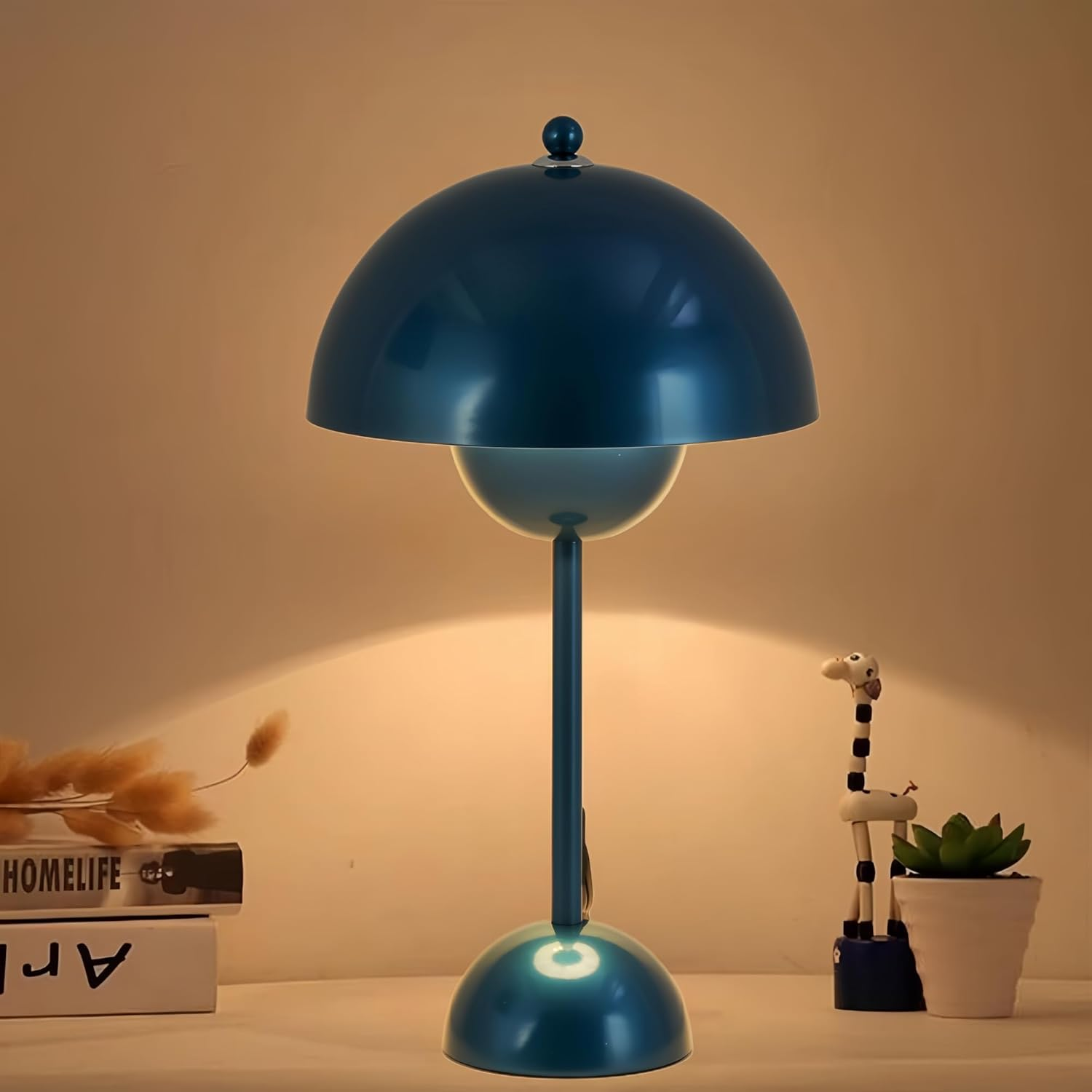 Lámpara de mesa azul sobre mesa blanca, con libros y figura de jirafa.