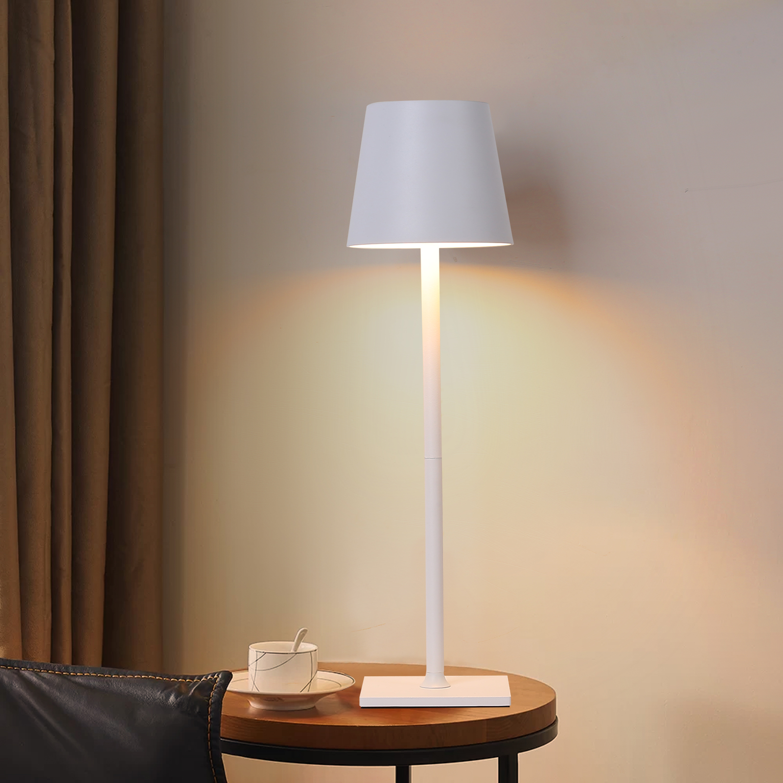 Una lámpara blanca sobre una base blanca. La lámpara está sobre una mesa de madera con una taza y platillo.