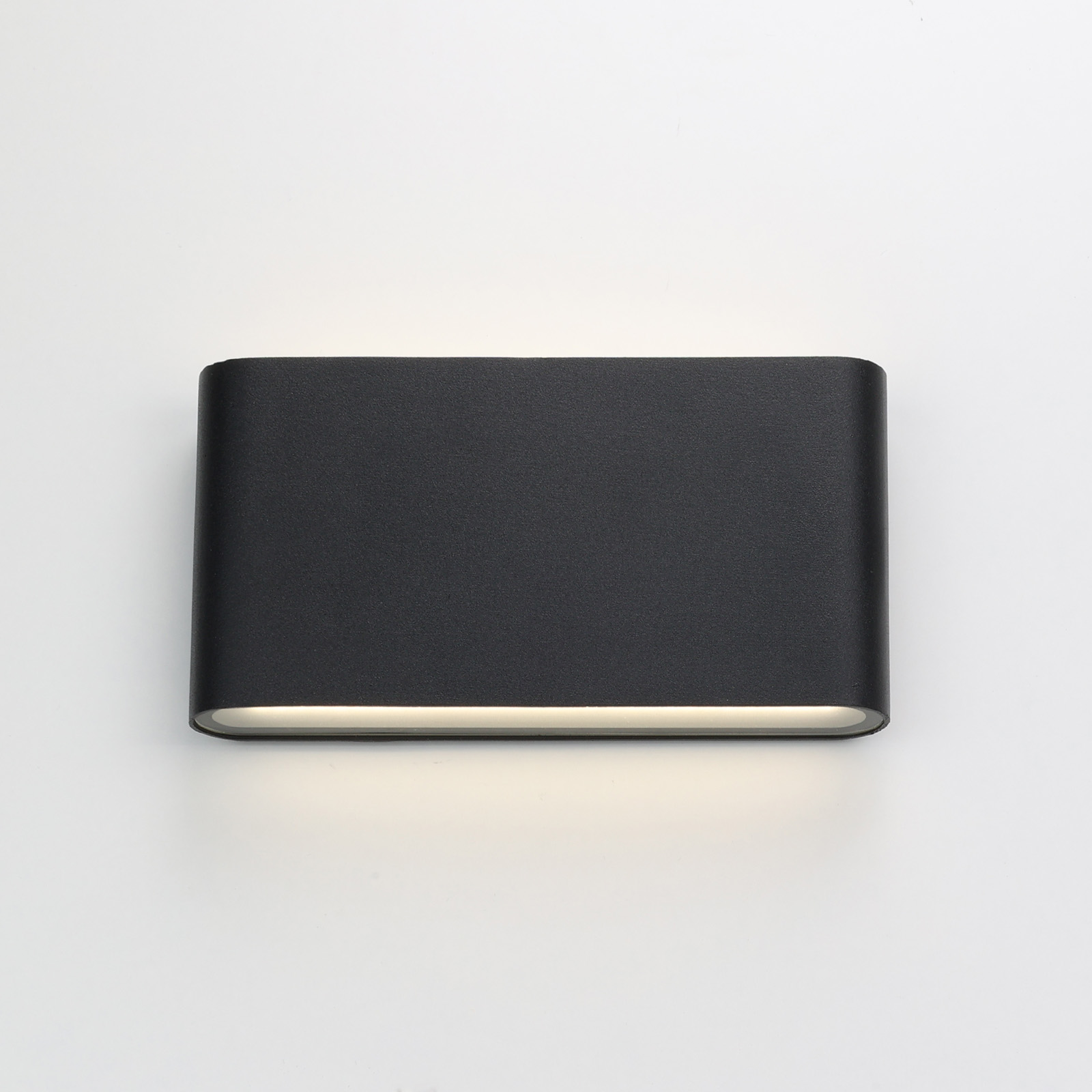 Una lámpara de pared rectangular negra sobre un fondo blanco. La lámpara está encendida.