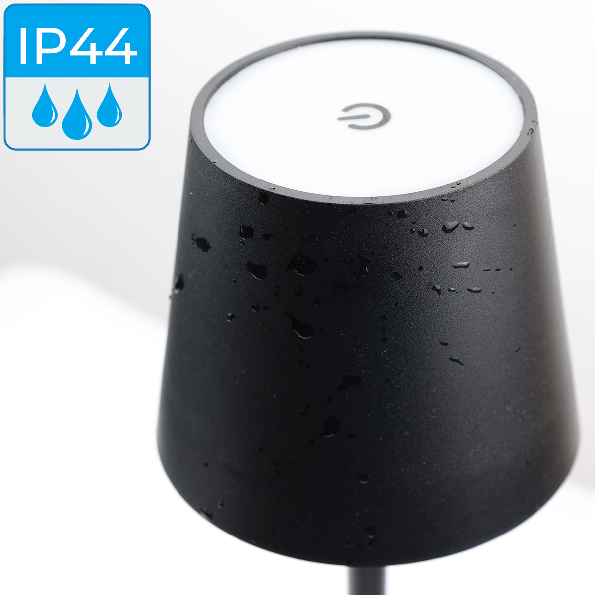 Primer plano de una lámpara negra con gotas de agua en su superficie. El icono IP44 impermeable está en la esquina.