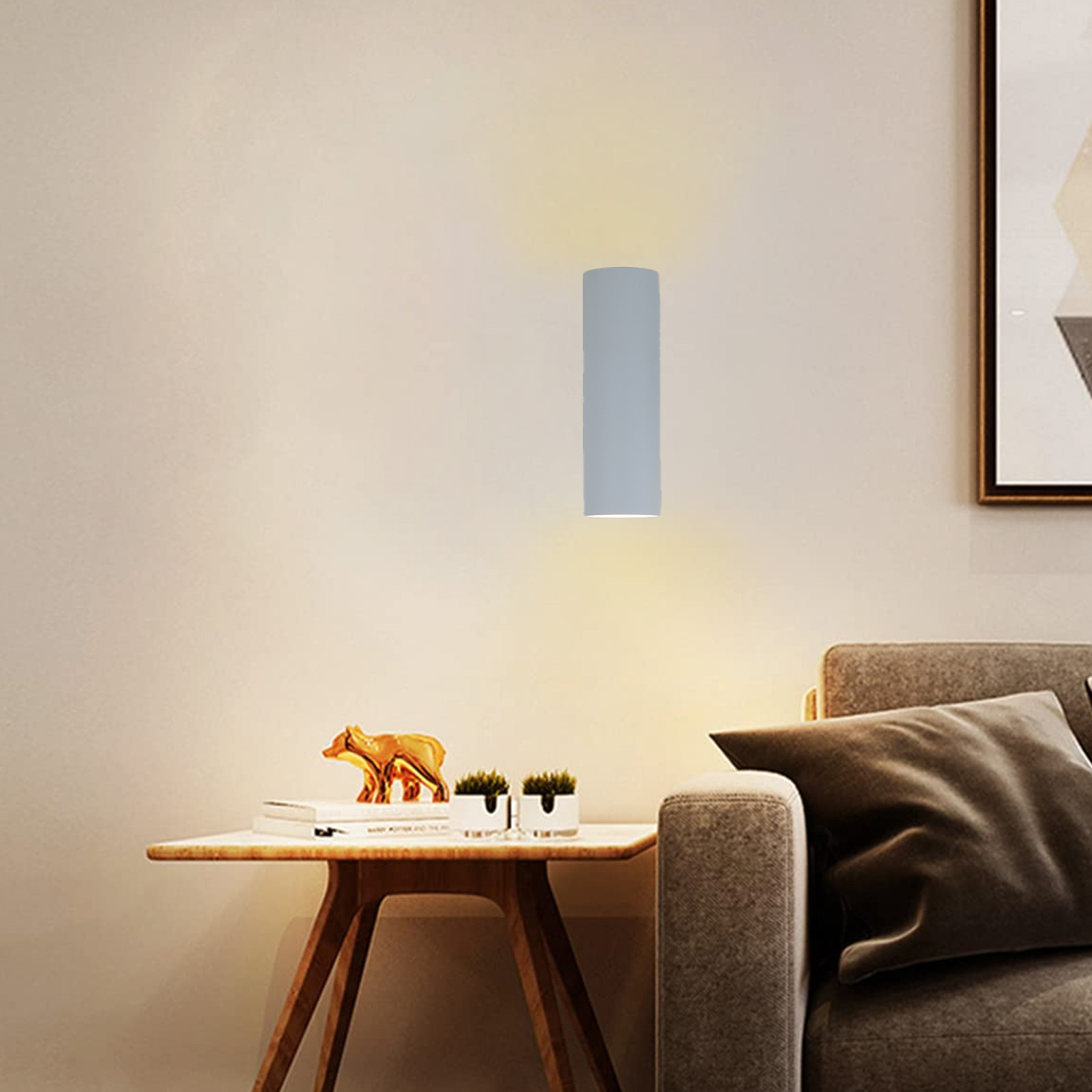 Una lámpara de pared cilíndrica gris montada en una pared beige, cerca de un sofá y una mesa. Estatua de oso dorada.
