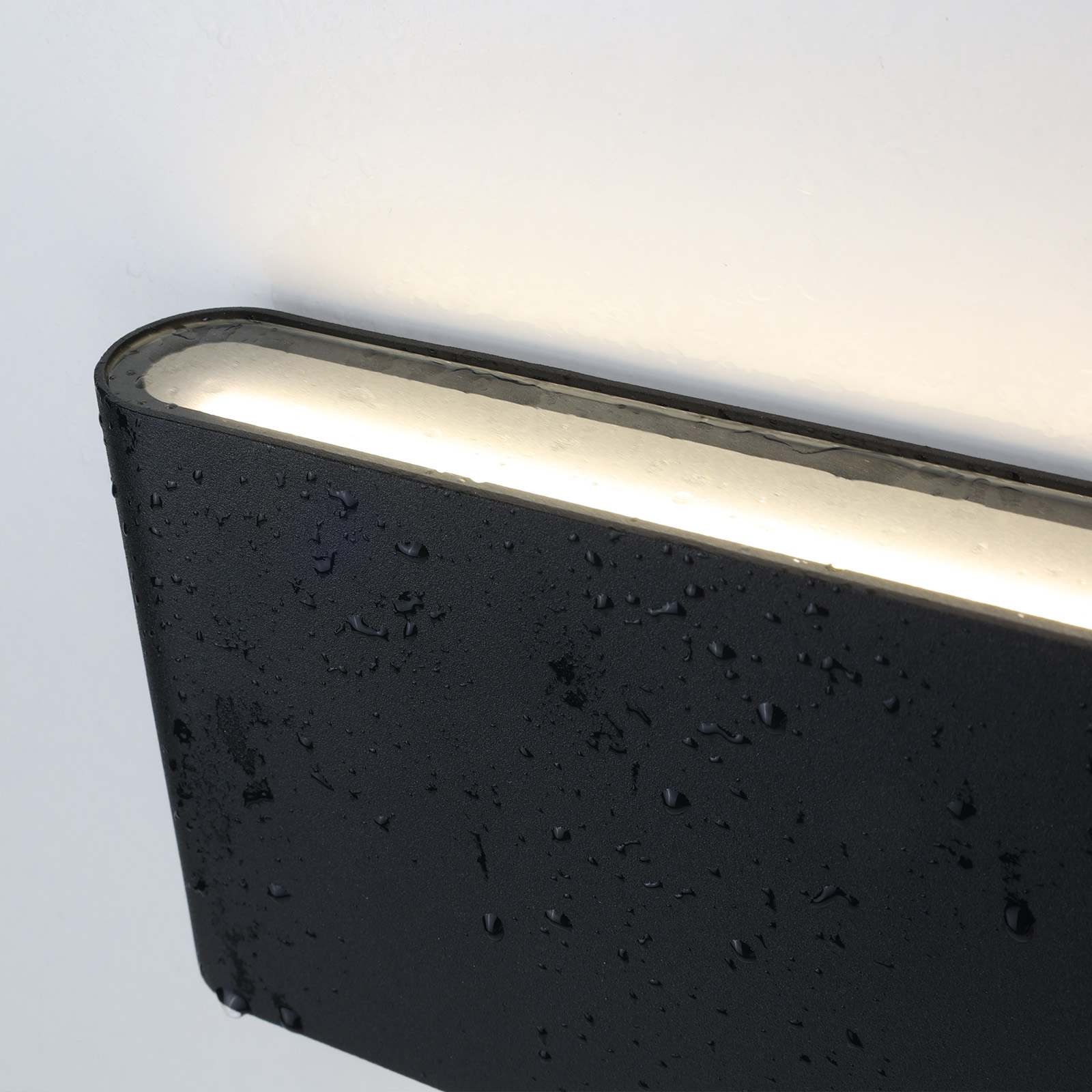 Una lámpara de pared negra. La luz está encendida y gotas de agua son visibles en la superficie.