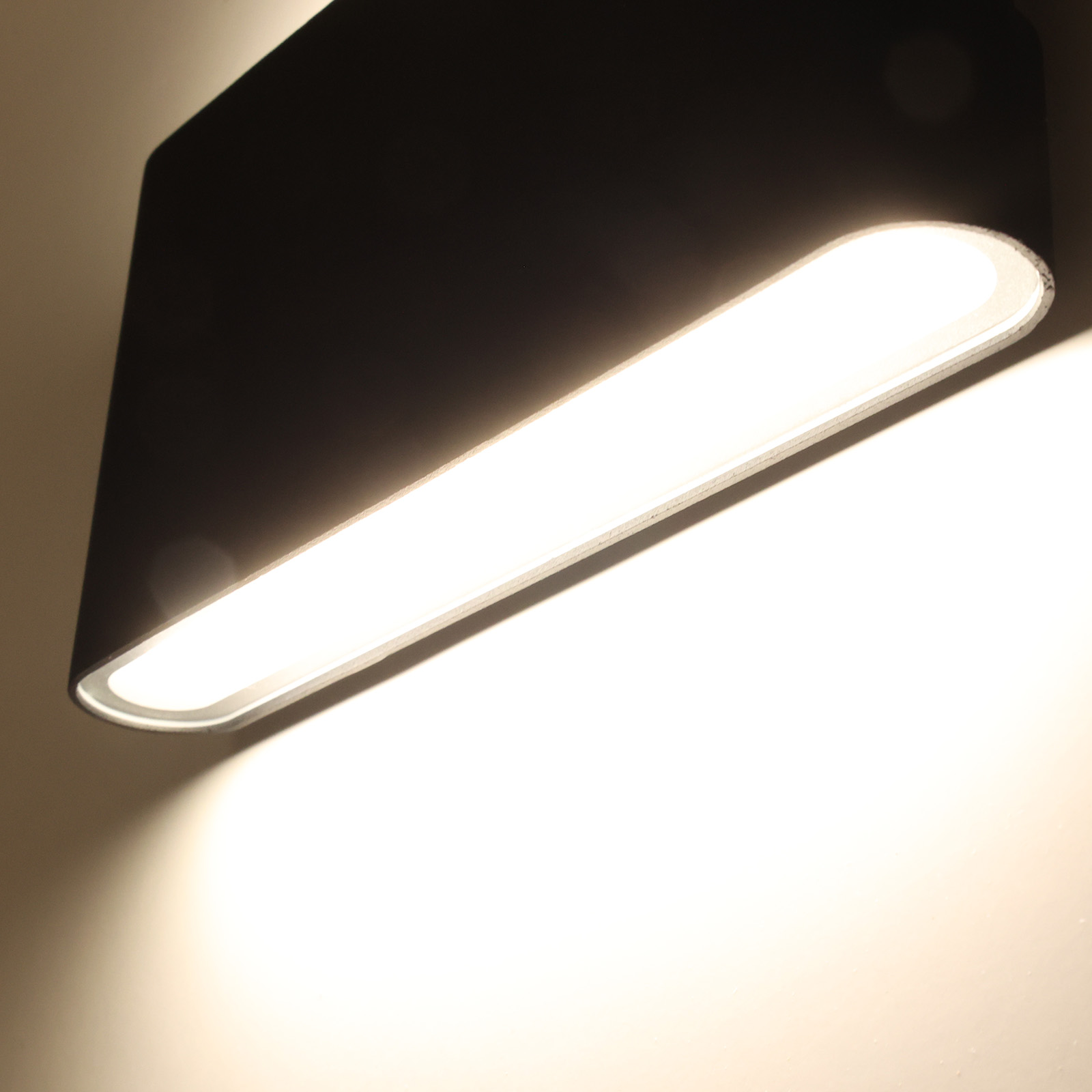 Primer plano de una lámpara de pared exterior negra, que emite una luz blanca brillante.