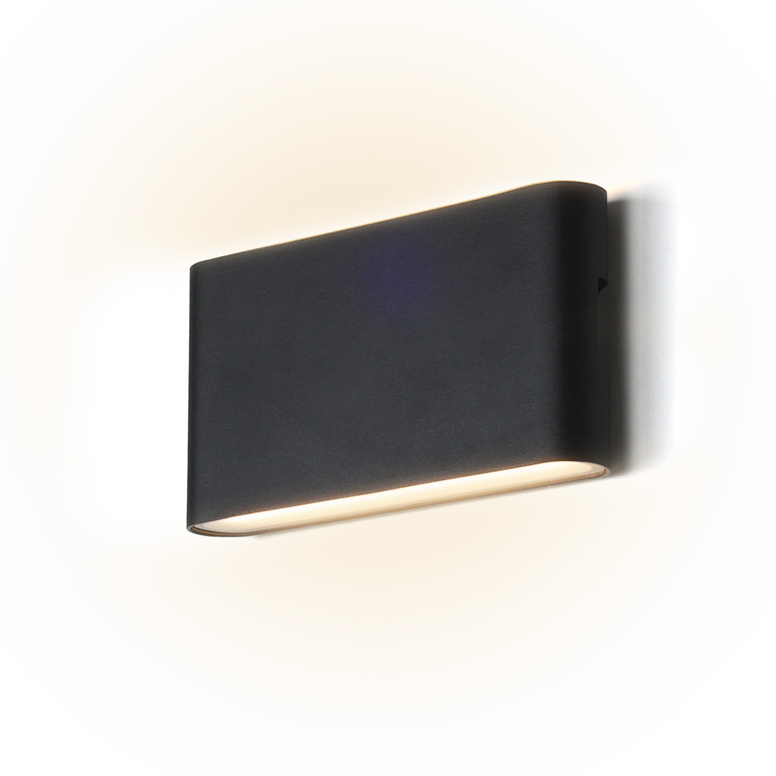Una lámpara de pared exterior negra en una pared blanca. Está emitiendo una luz blanca cálida.