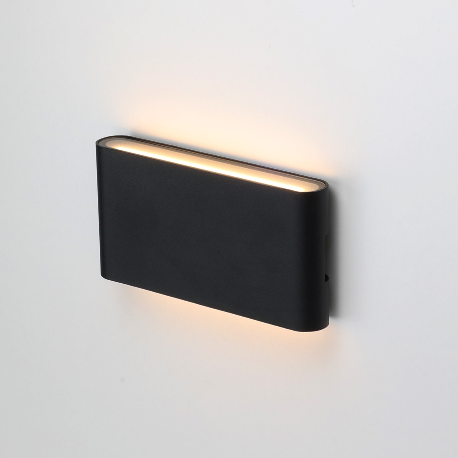 Una lámpara de pared negra. La luz está encendida y la lámpara está montada en la pared.