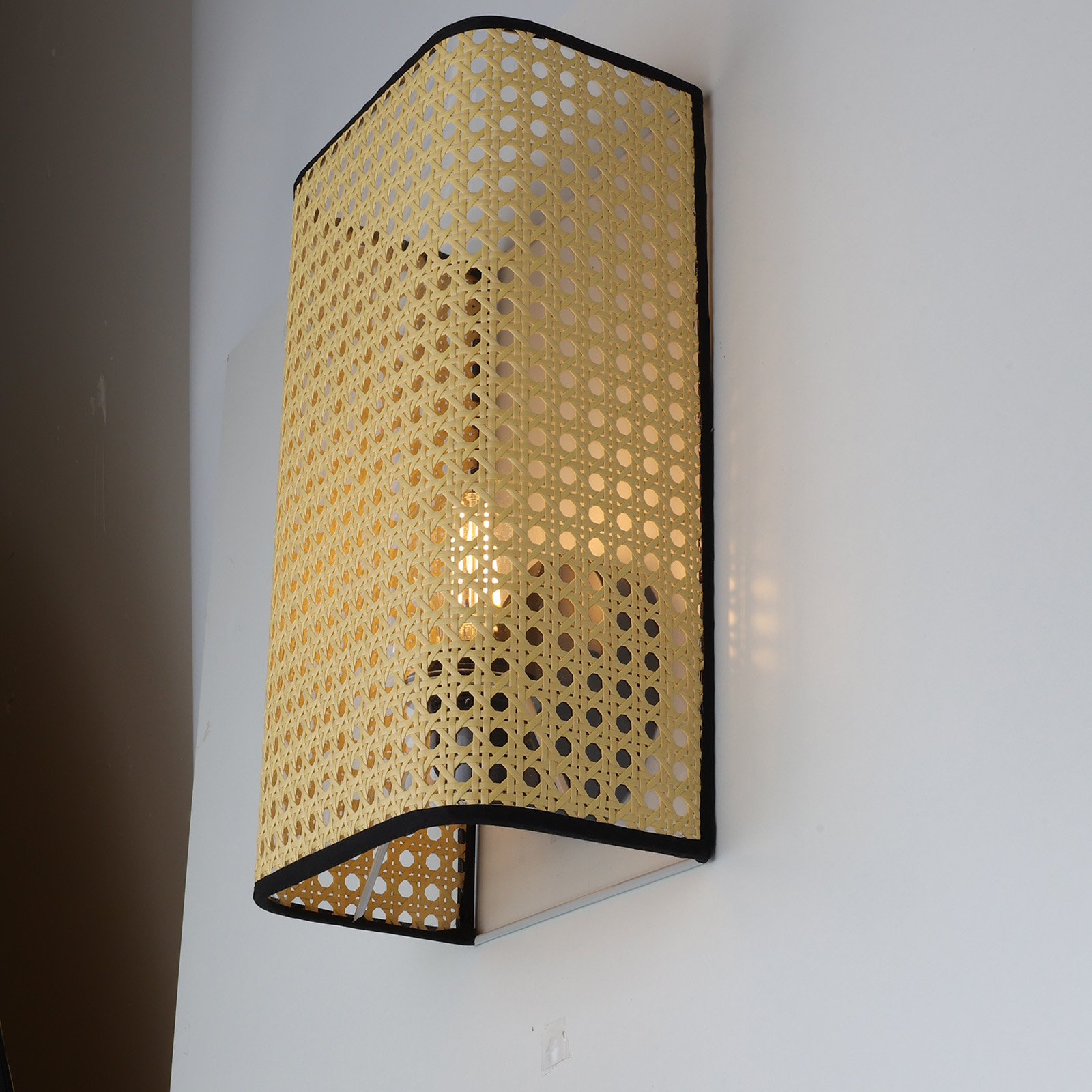 Una lámpara de pared de ratán con borde negro sobre una pared blanca.