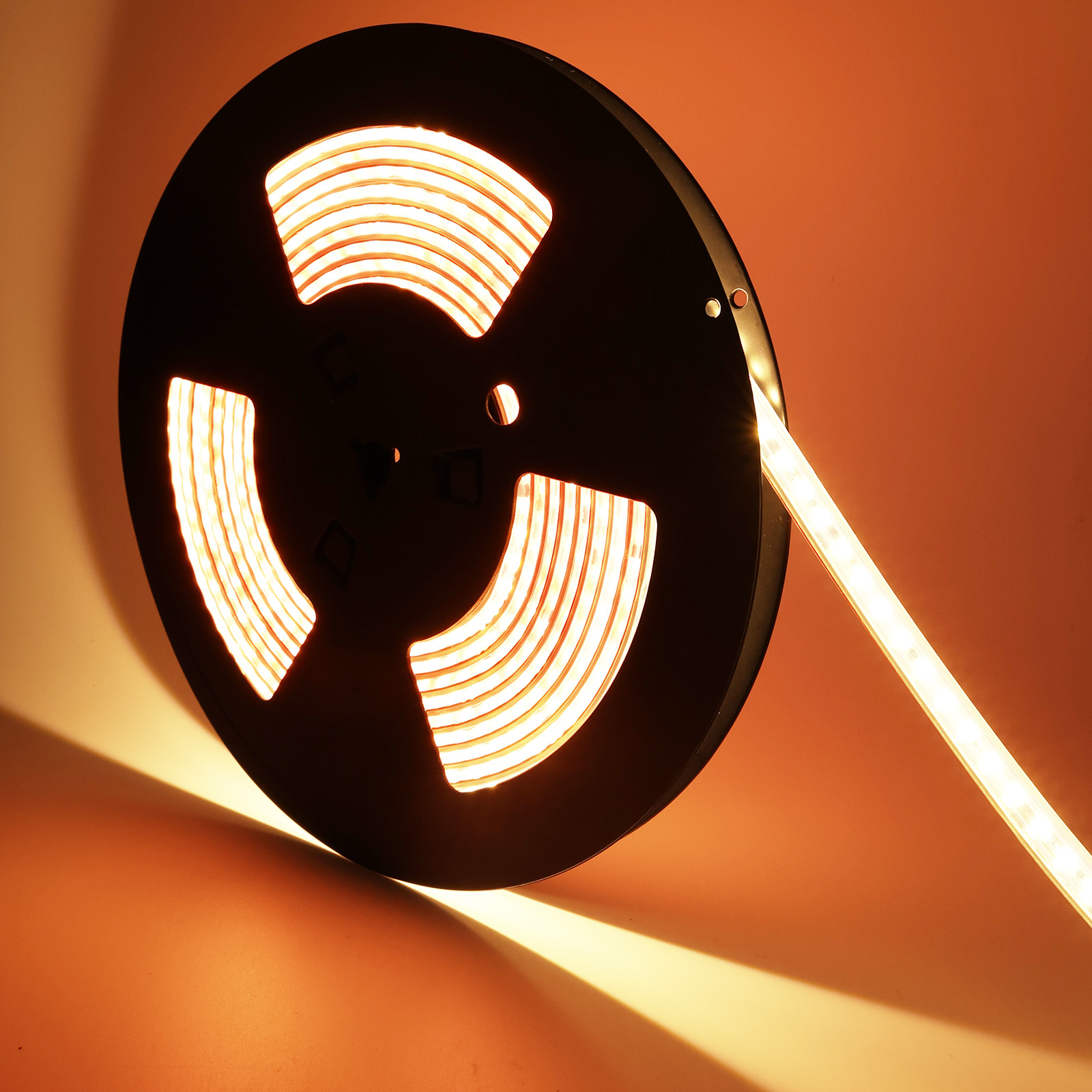 Una bobina de tiras de luces LED, con una sección extendida, mostrando luz cálida anaranjada.