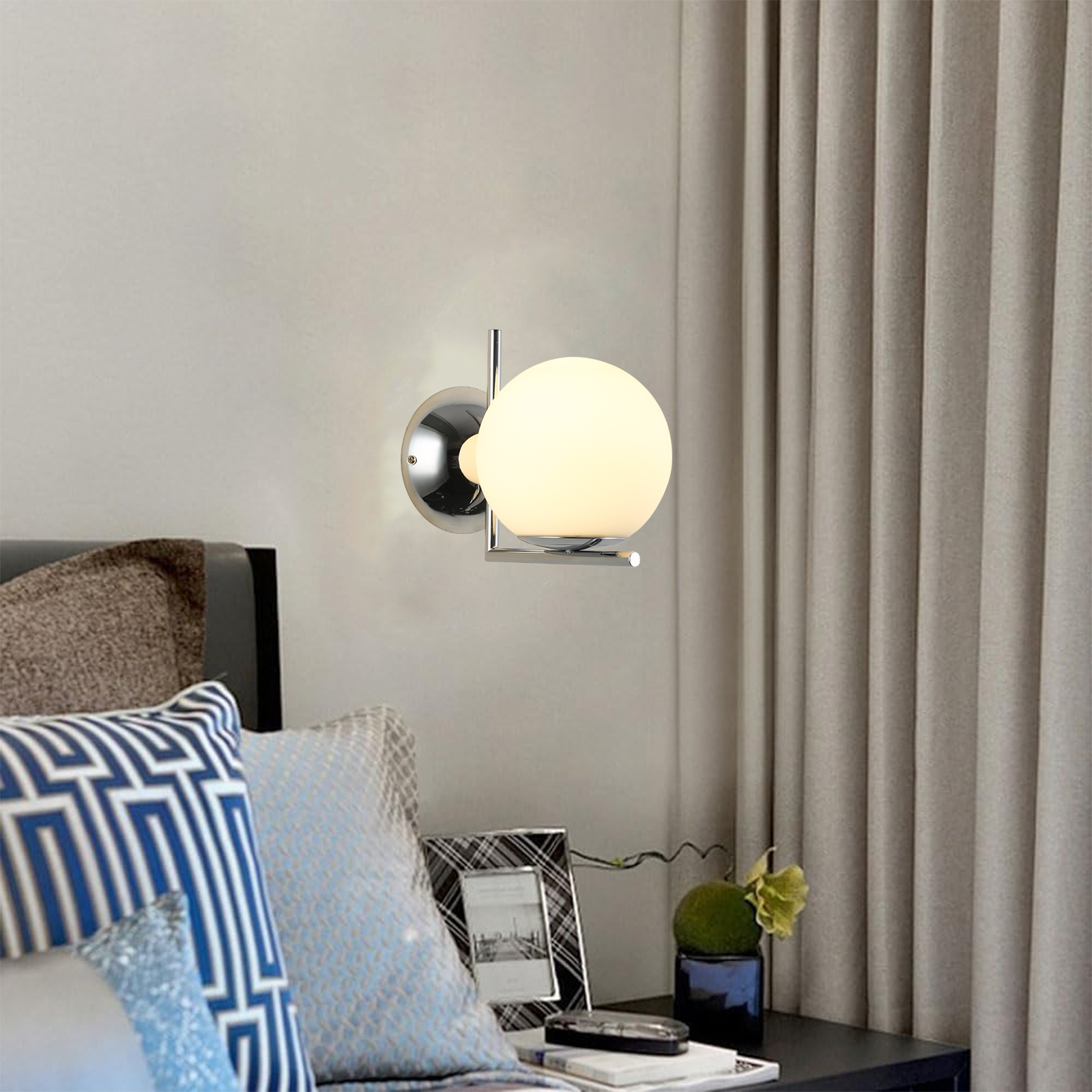 Lámpara de pared con base cromada y pantalla de vidrio esférica esmerilada, junto a una cama y cortinas.