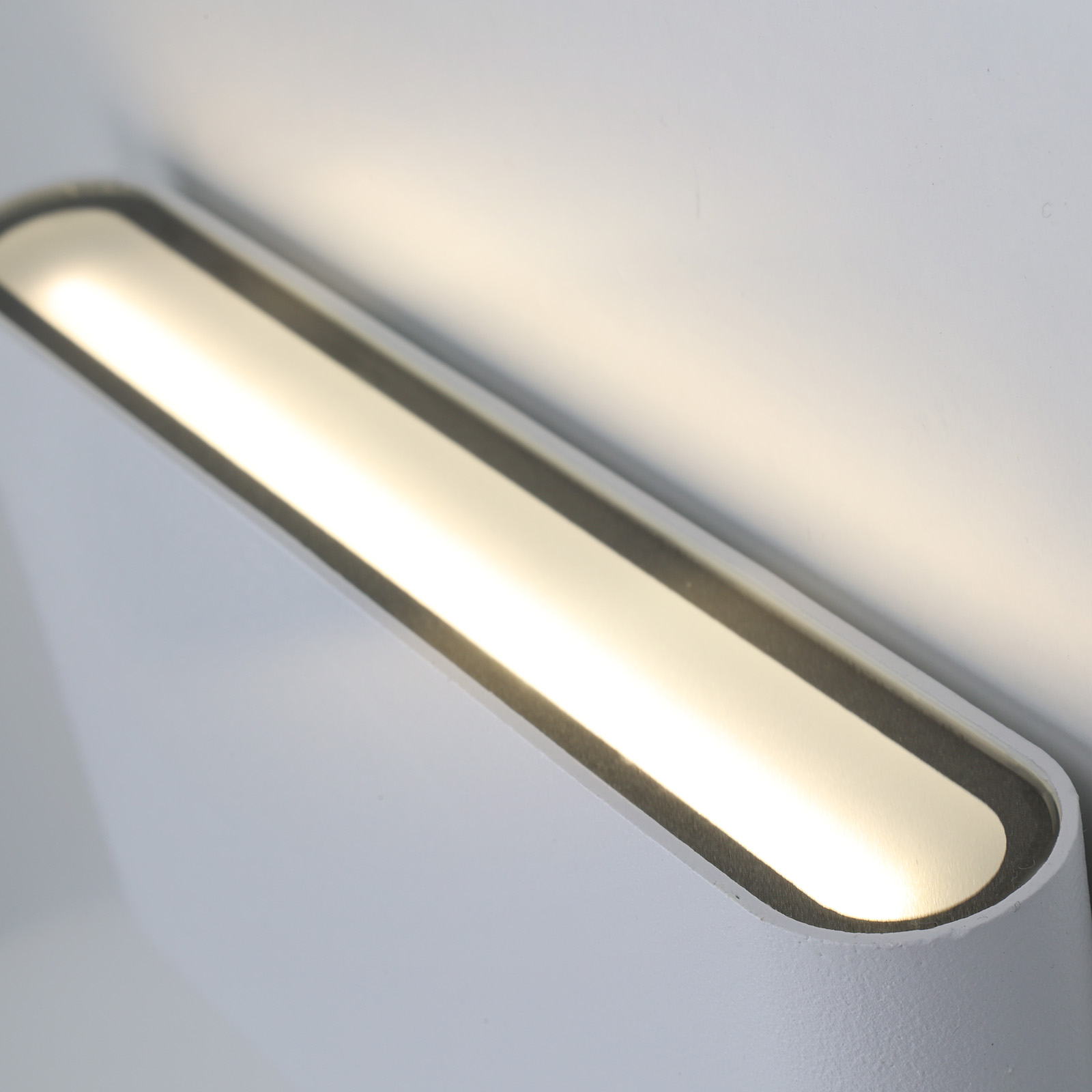 Una lámpara de pared blanca con una luz brillante que emana de la parte delantera. La lámpara está inclinada hacia arriba.
