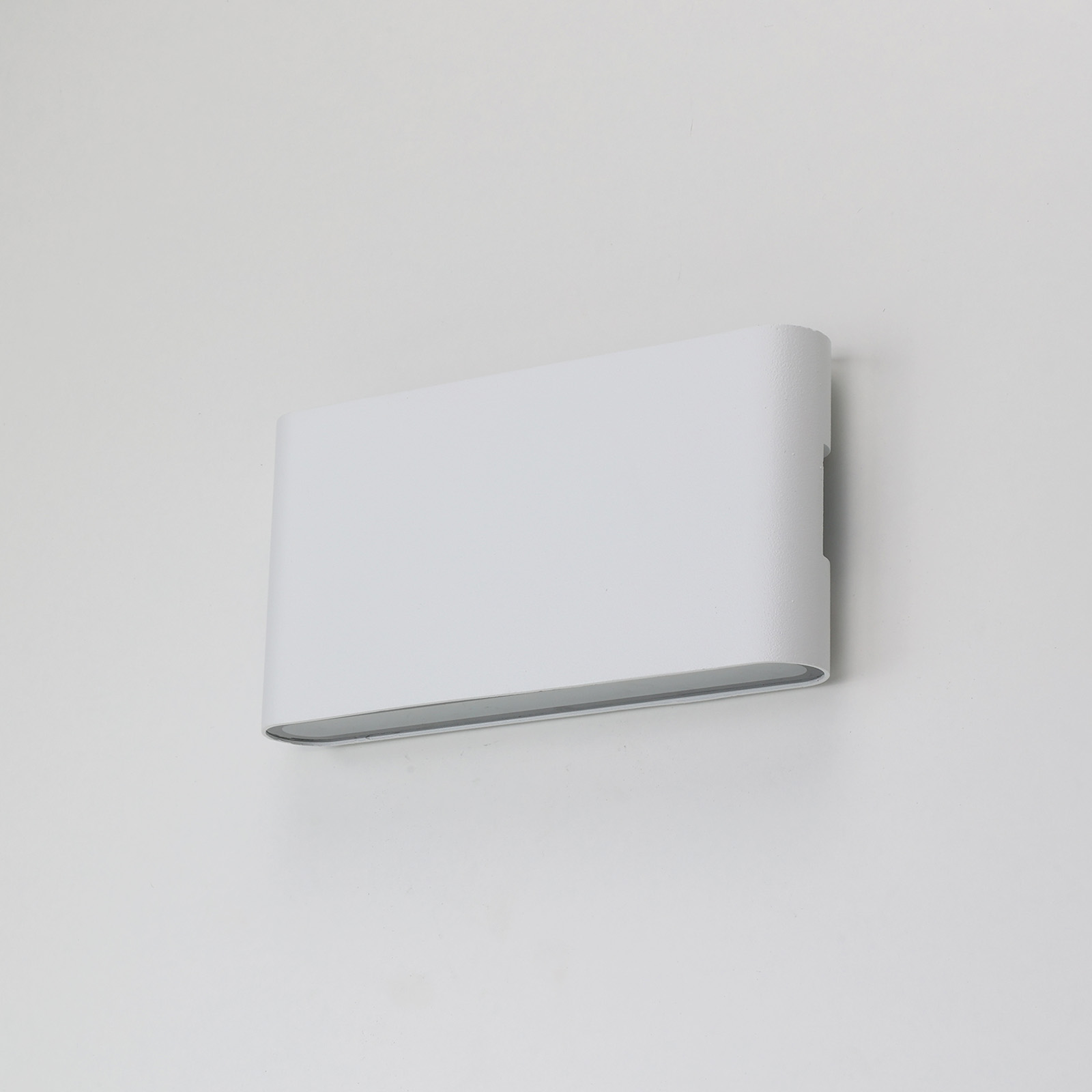 Una lámpara de pared blanca con forma rectangular. Está montada en una pared blanca.