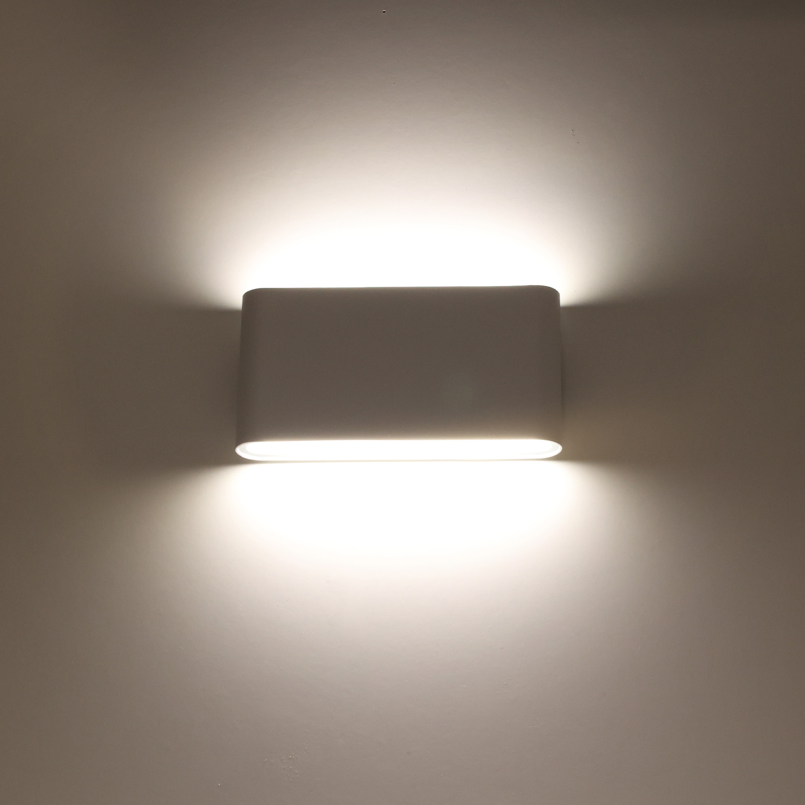 Una lámpara de pared blanca con una luz brillante y cálida que brilla hacia abajo sobre una pared.