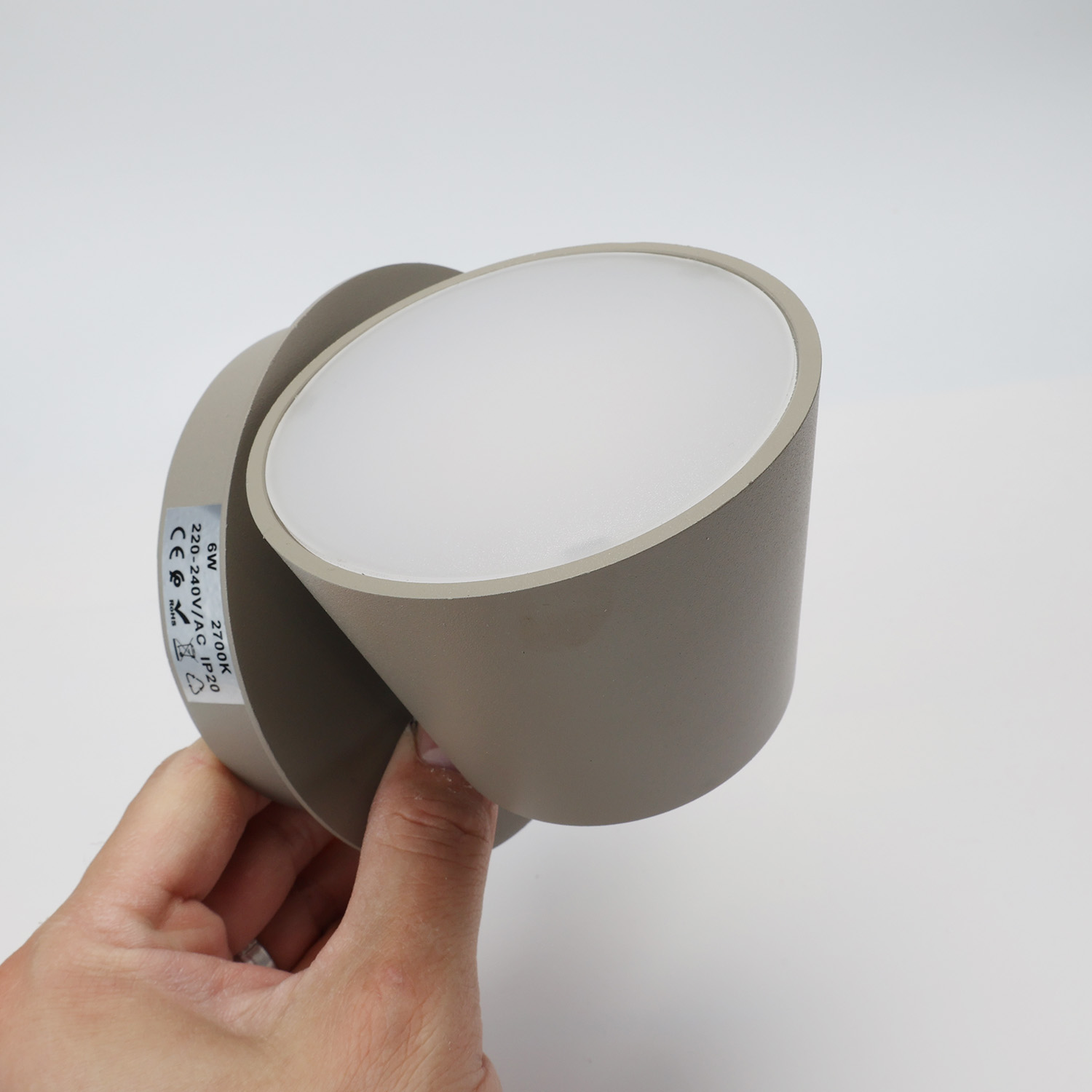 Una mano sostiene una lámpara de pared gris. Tiene una forma redondeada con una superficie emisora de luz.