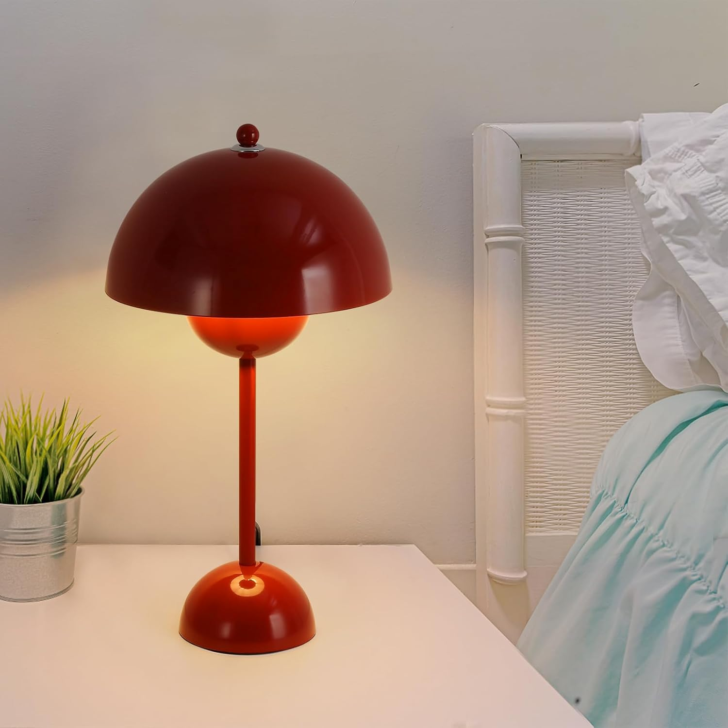 Lámpara de mesa roja con pantalla en forma de cúpula, sobre mesa blanca, junto a una planta.