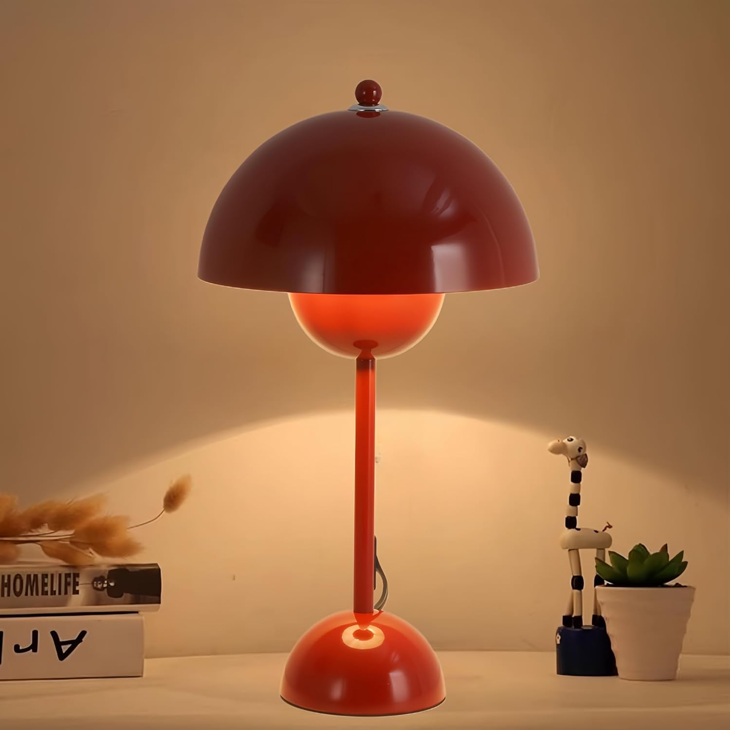 Una lámpara de escritorio roja con base y pantalla redondas, más una jirafa y una planta.