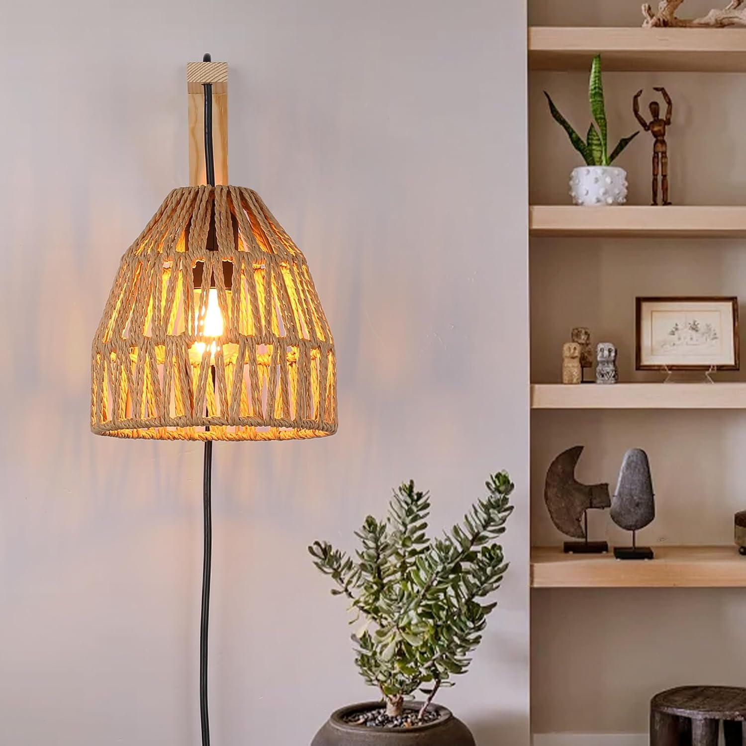 Una lámpara de pared con una pantalla de ratán, un soporte de madera y una planta. El fondo es una pared y estantes.