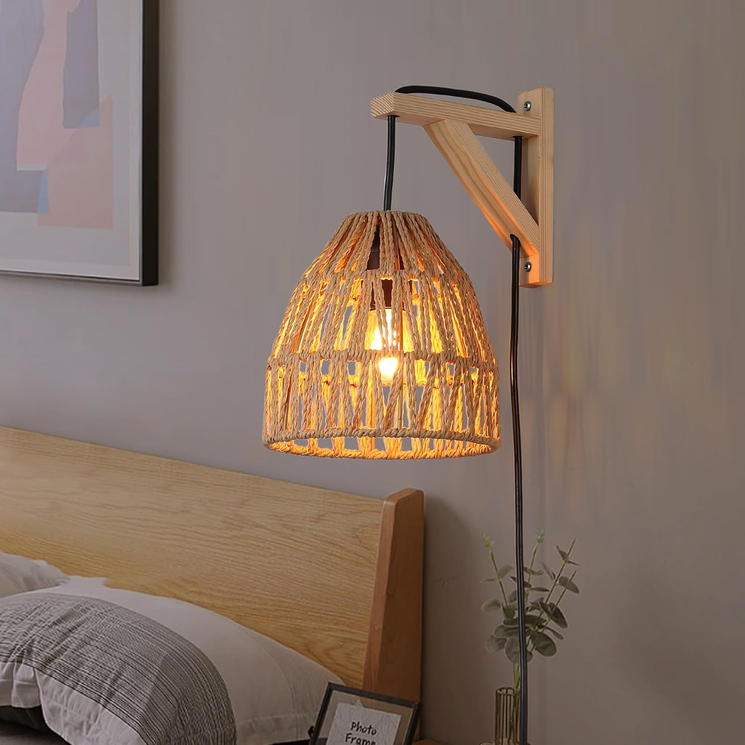 Lámpara de pared con pantalla tejida, soporte de madera y cable negro.