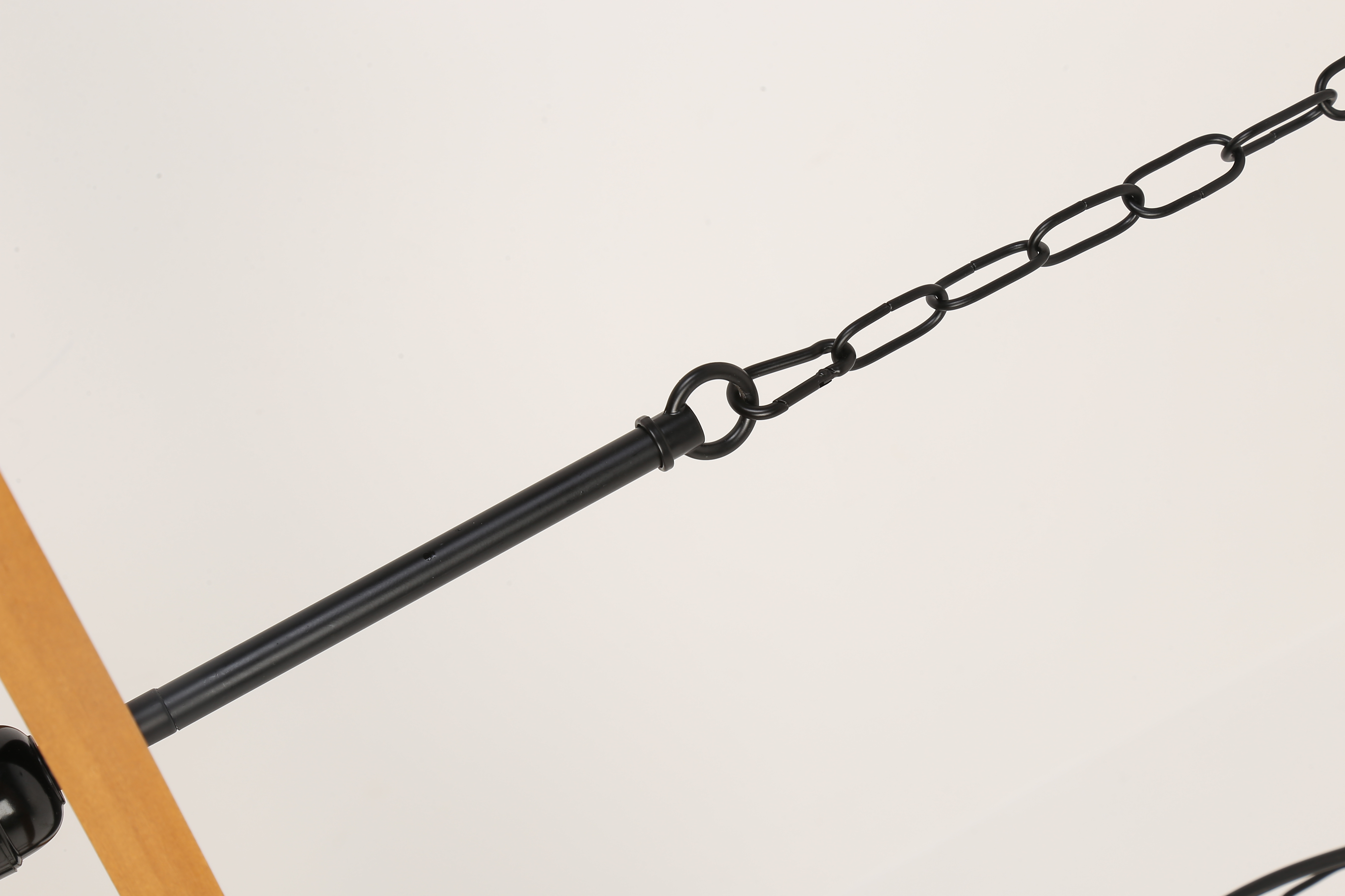 Primer plano de una cadena conectada a una viga de madera que soporta una lámpara.