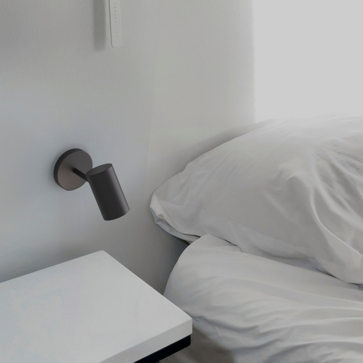 Lámpara de pared moderna, gris oscuro, junto a una mesita de noche blanca y una cama con sábanas blancas.
