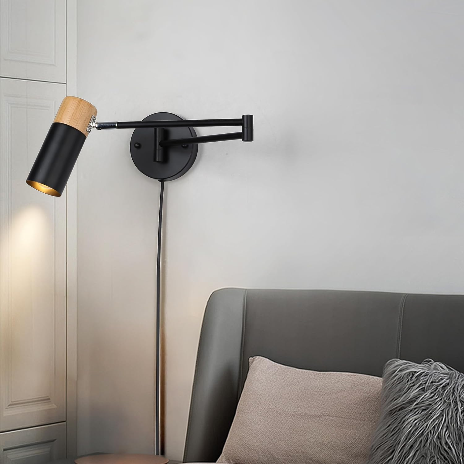 Una lámpara de pared negra y de madera está montada en una pared blanca. La lámpara tiene un brazo ajustable y está encendida.