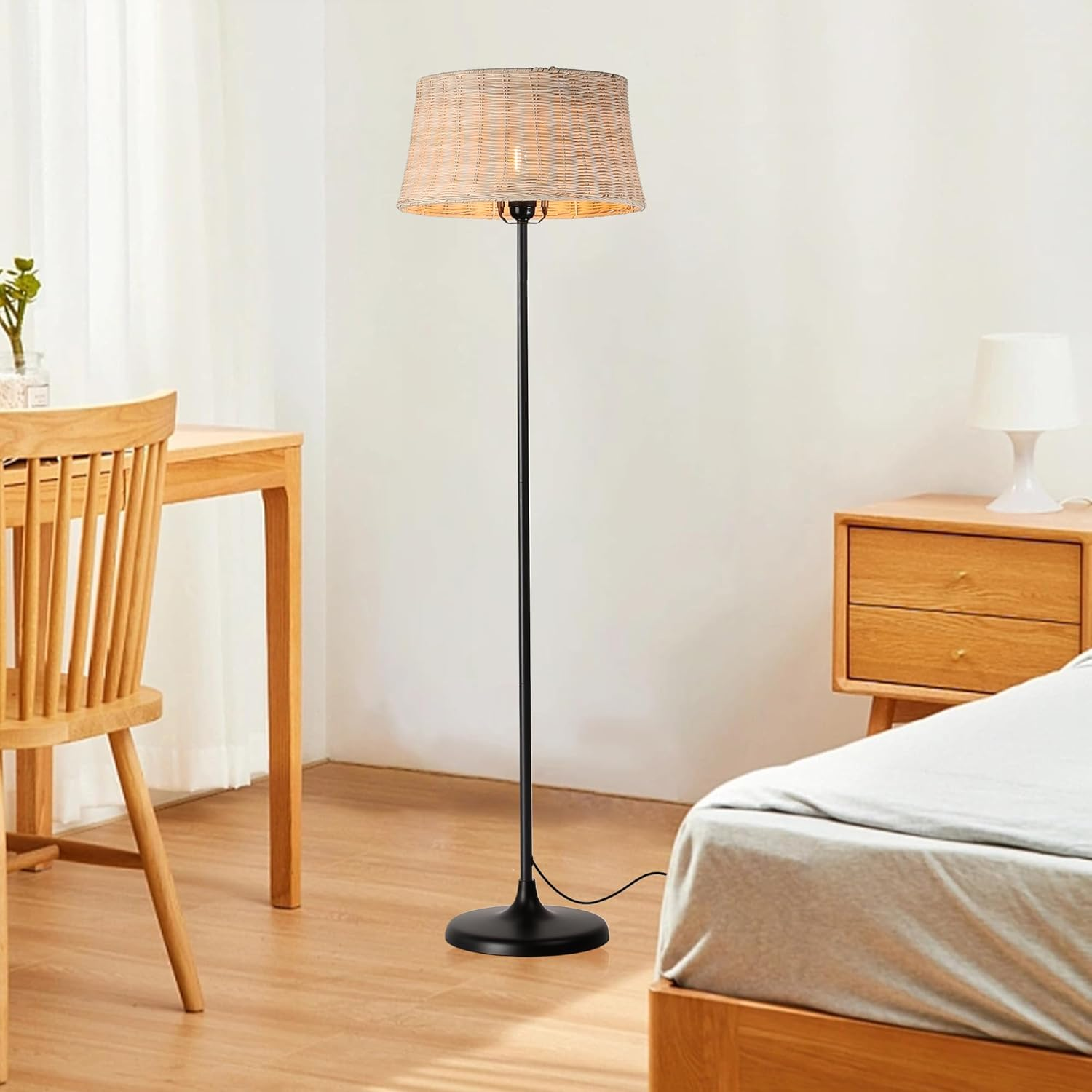 Una lámpara de pie con pantalla tejida, cerca de una cama.