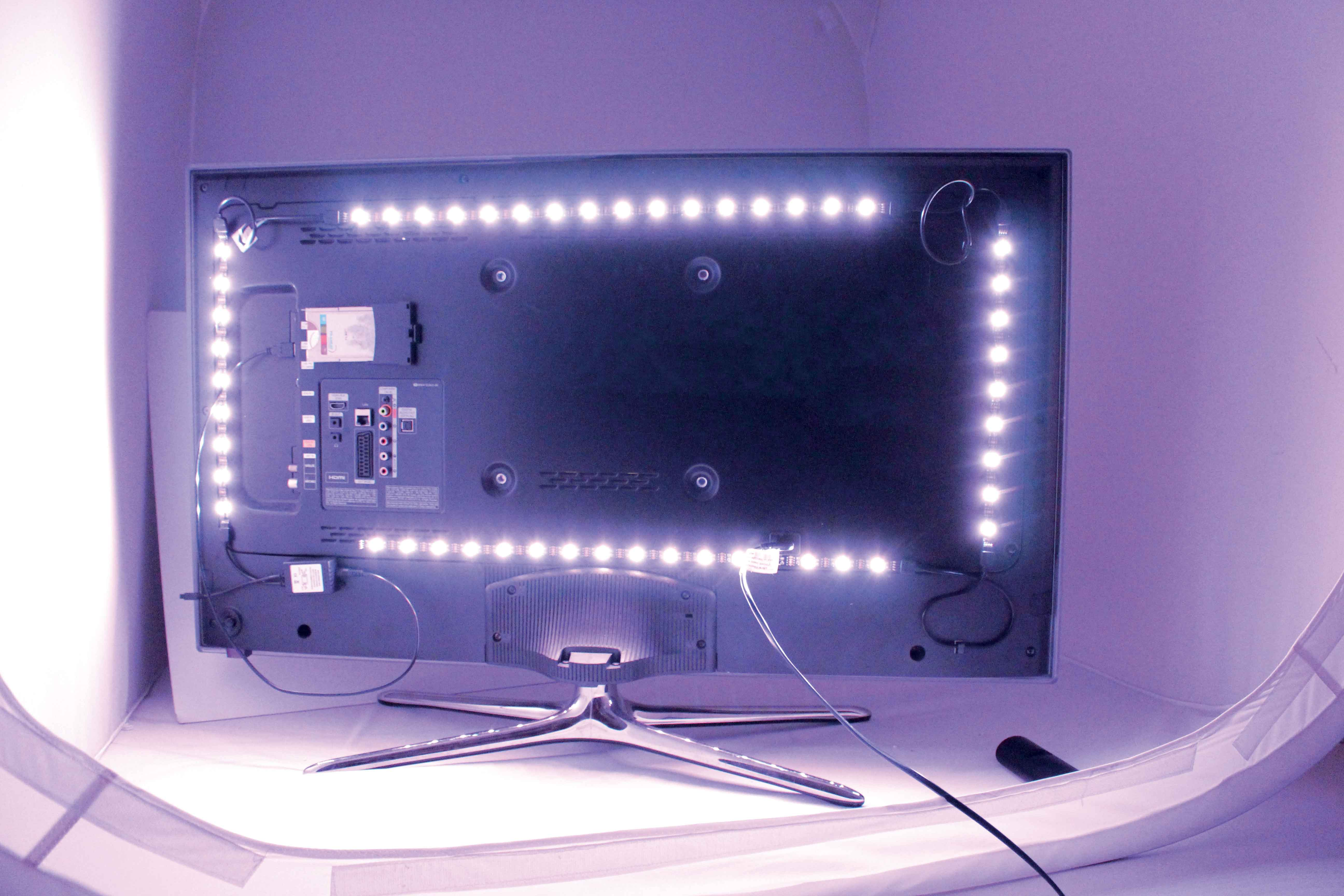 Parte trasera del televisor con tiras de luces LED. Cables, puertos y soporte presentes. Estudio.