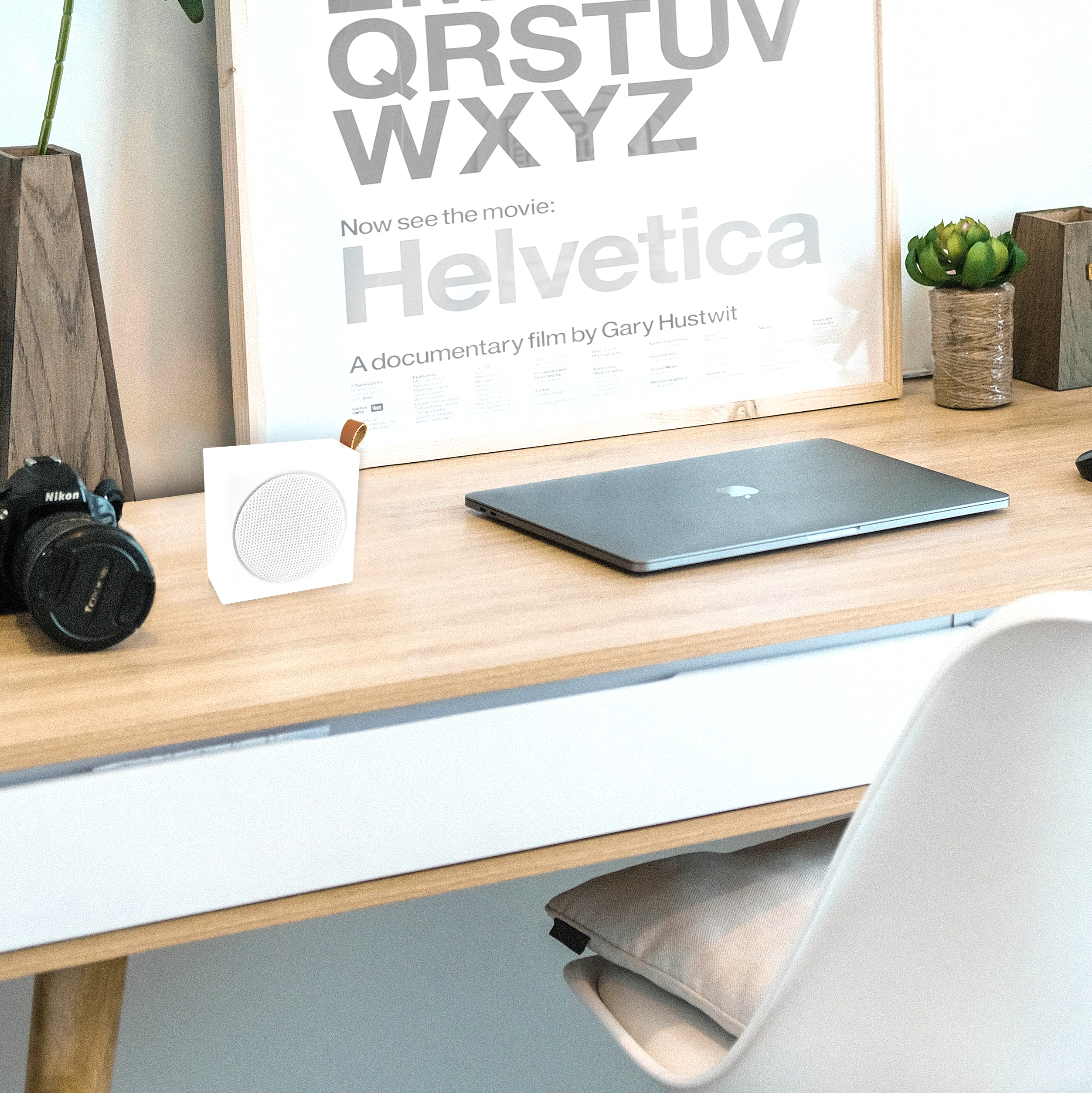 Un escritorio con un altavoz, una cámara, una computadora portátil y un póster que dice Helvetica.