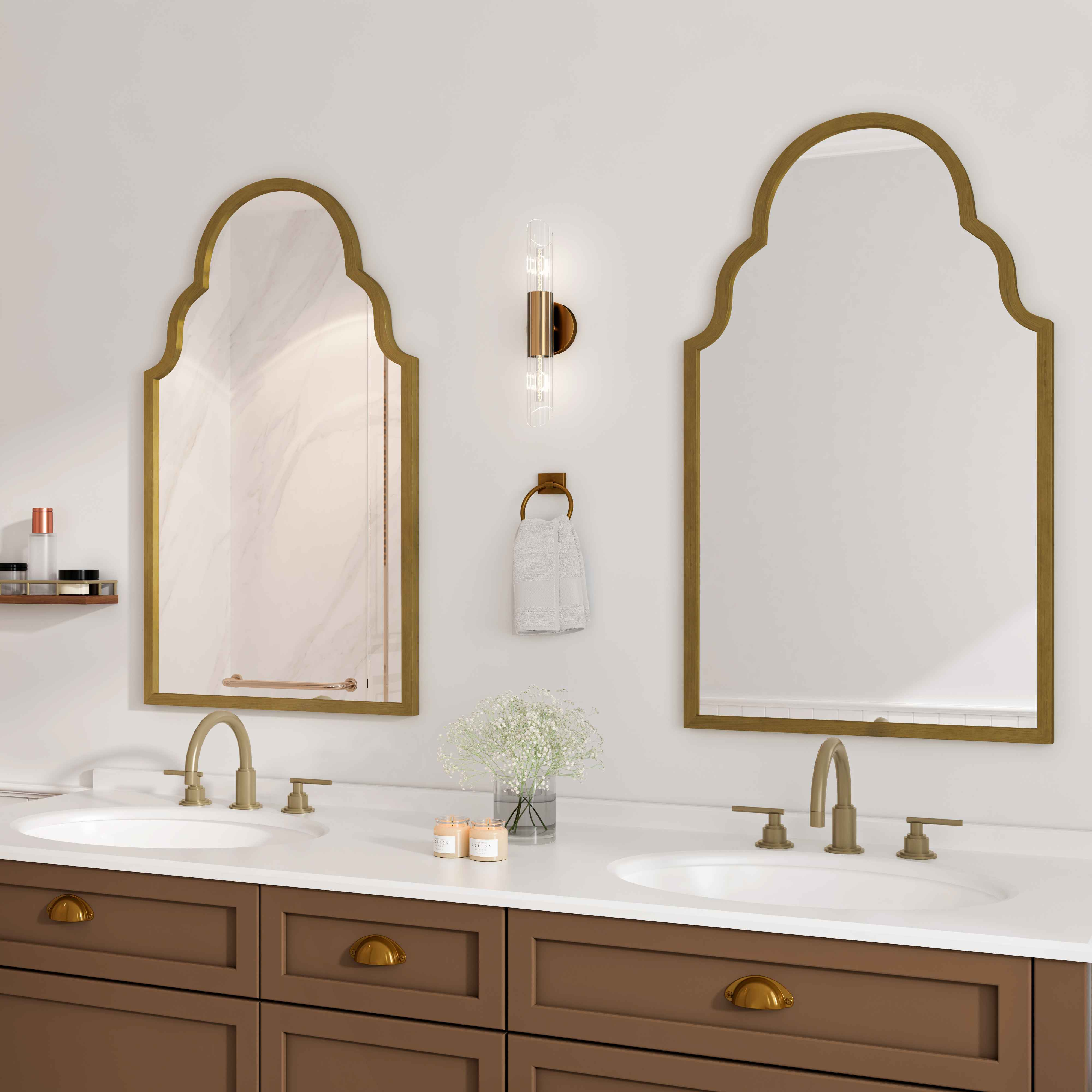 Ein Badezimmer mit zwei goldgerahmten Spiegeln. Es gibt ein Regal mit Produkten, ein Waschbecken, ein Handtuch, Blumen und einen braunen Schrank.