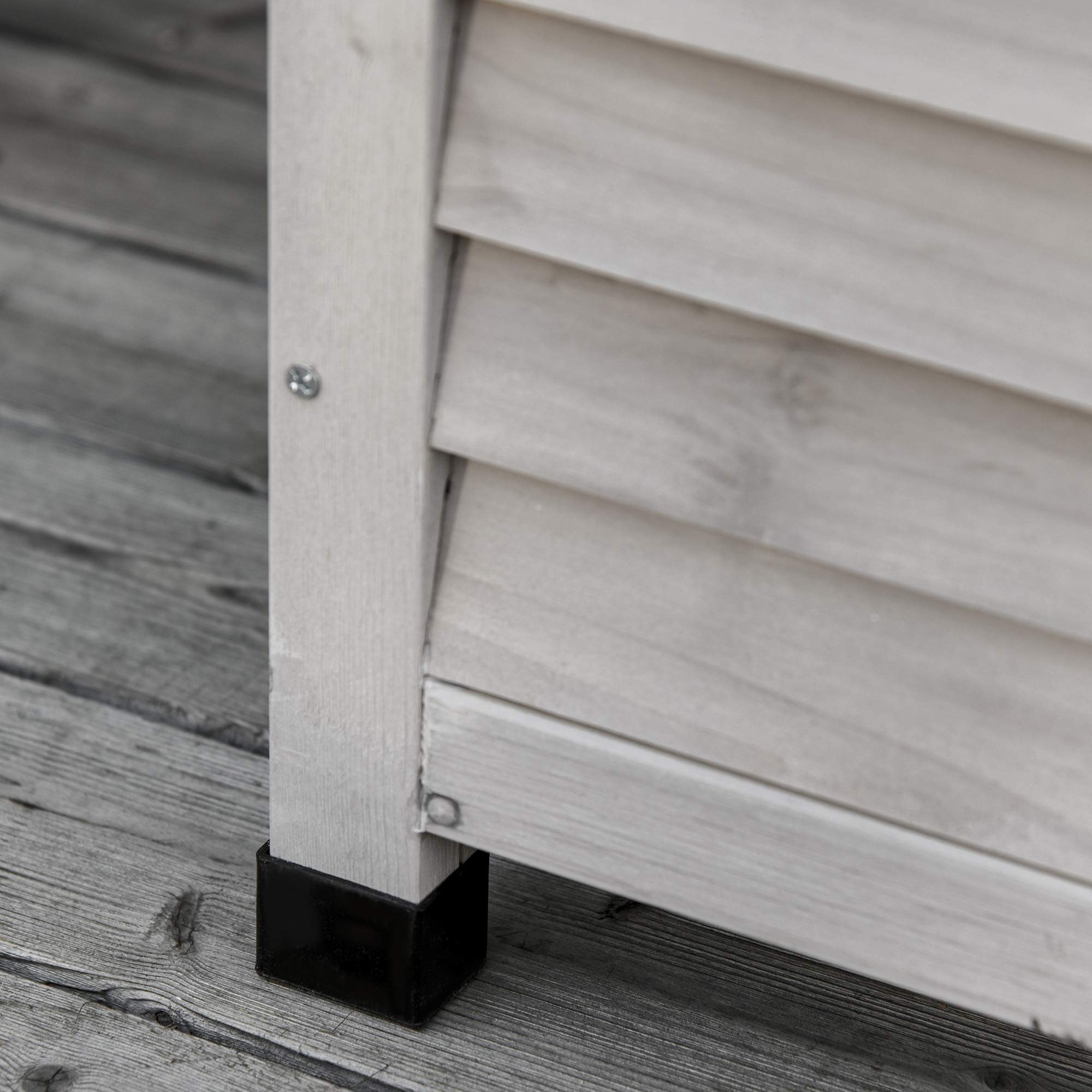 Nahaufnahme eines Holzaufbewahrungskastenbeins. Die Box ist hellgrau mit schwarzen quadratischen Füßen.