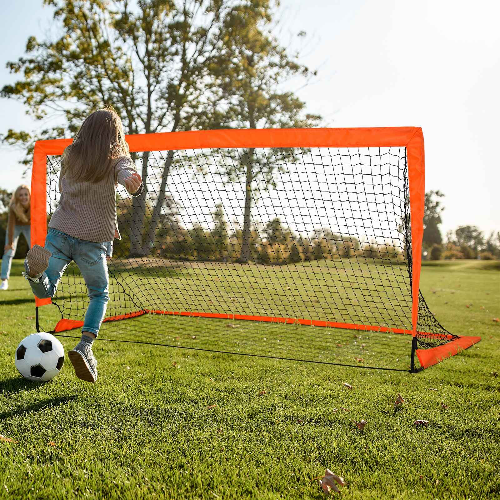 Ein Mädchen schießt einen Fußball in Richtung eines orangefarbenen Fußballtors auf einem grünen Feld.