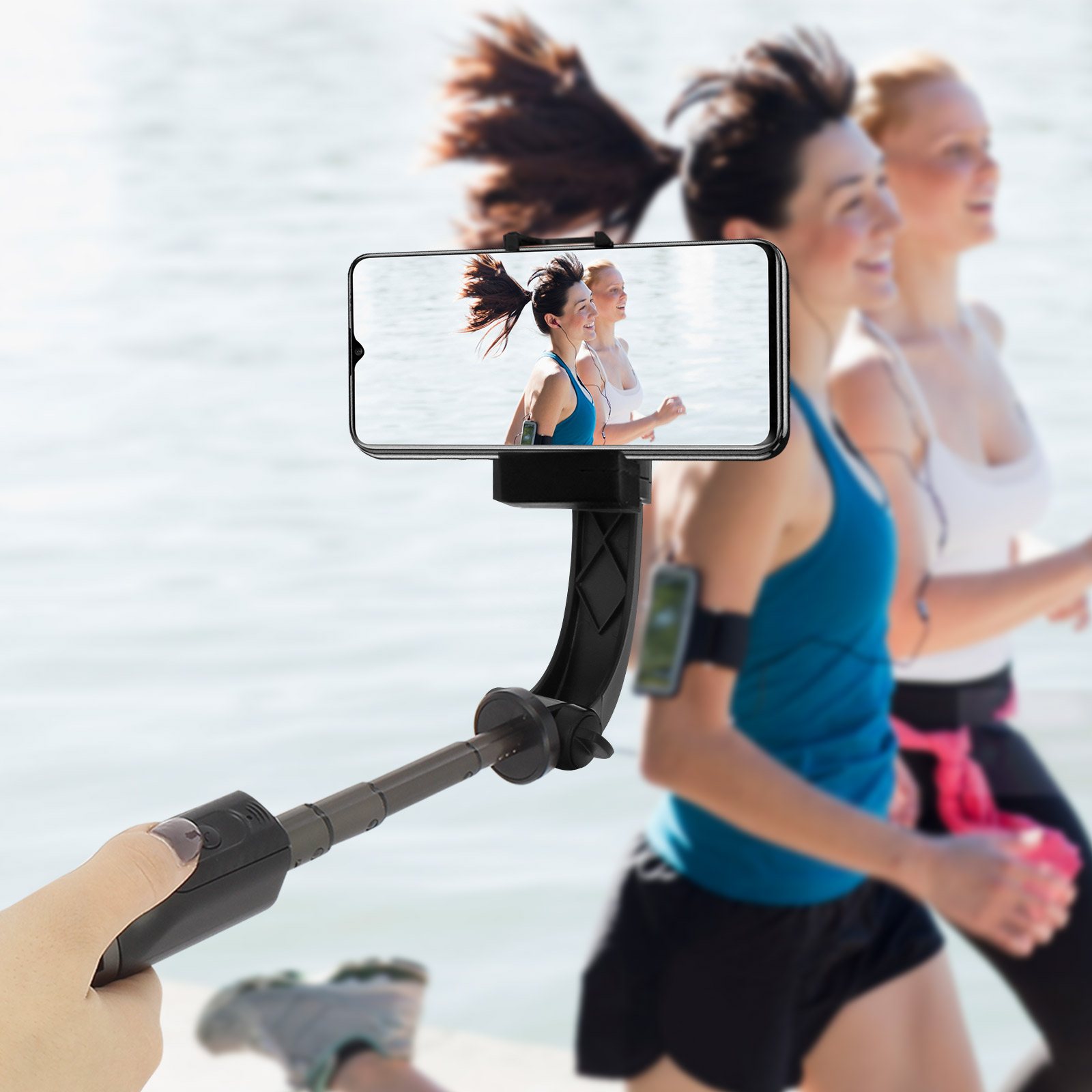 Un teléfono en un palo selfie captura a dos mujeres corriendo. El fondo es agua borrosa.
