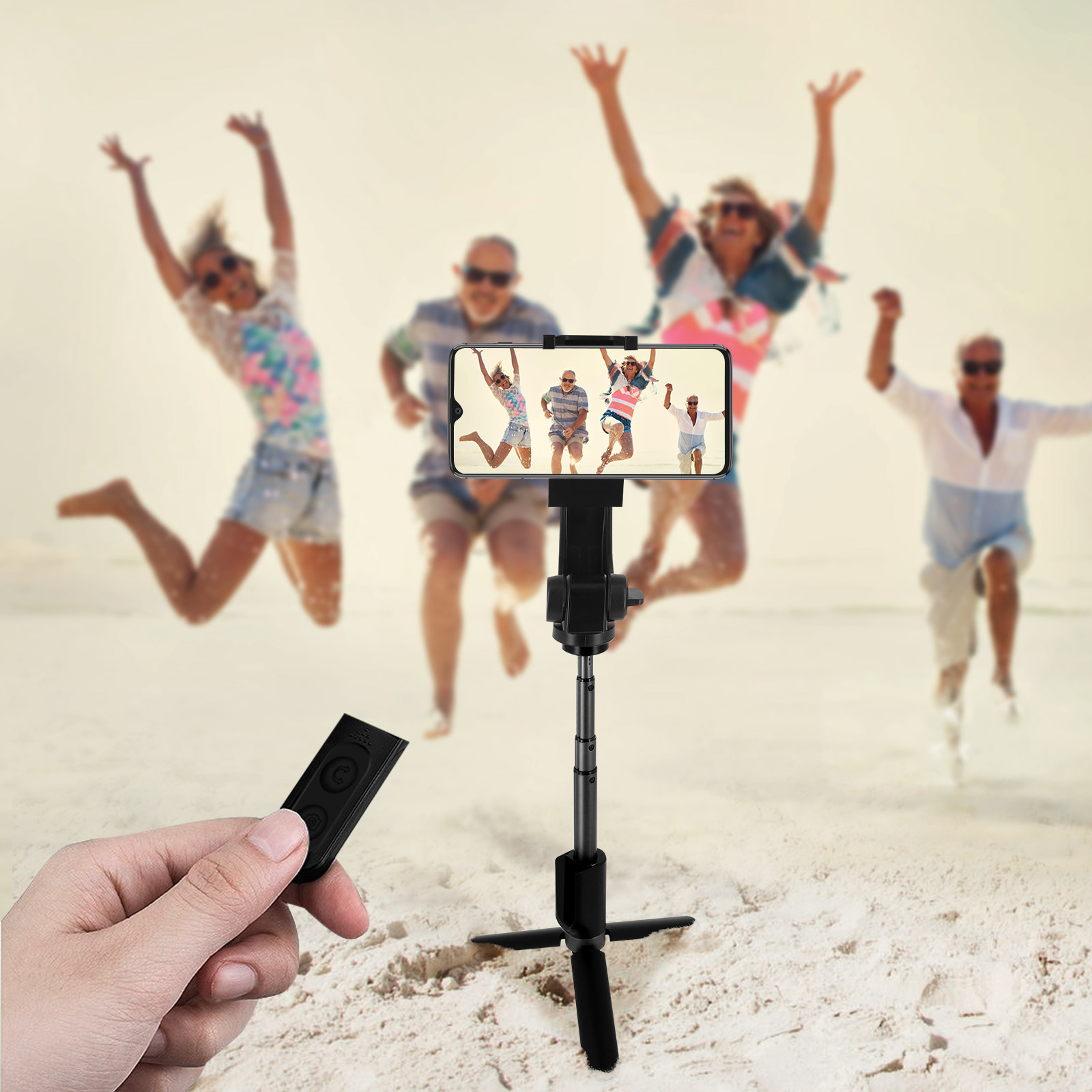 Personas haciendo una foto con un teléfono en un trípode. Un mando a distancia en primer plano en la playa.