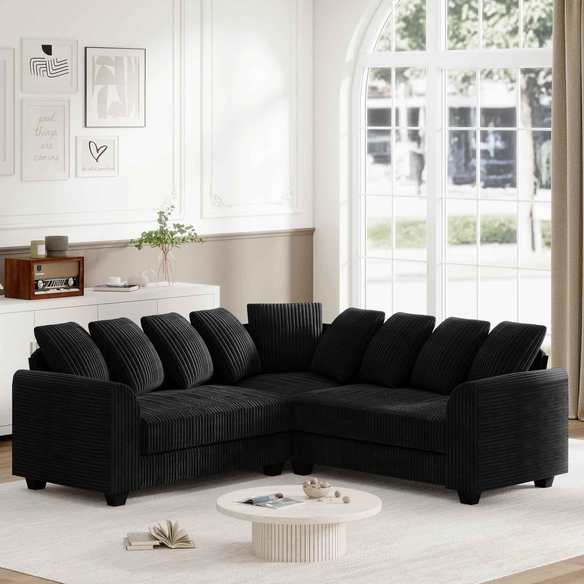 Schwarzes L-förmiges Sofa in einem gut beleuchteten Raum. Das Sofa steht vor einem Fenster und etwas Deko.