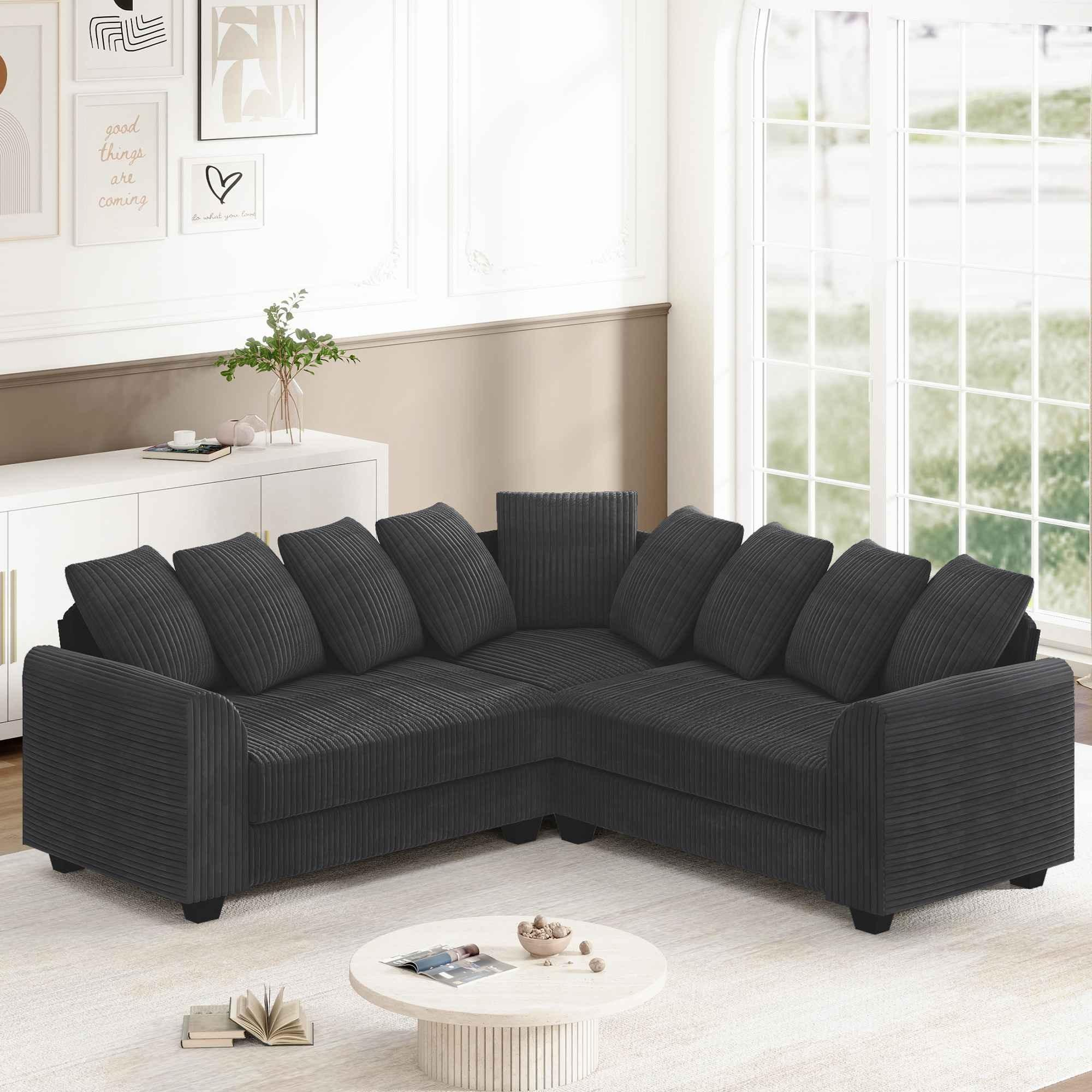 Dunkelgraues Ecksofa mit vielen Kissen auf hellem Teppich, in der Nähe eines weißen Beistelltisches und Fensters.