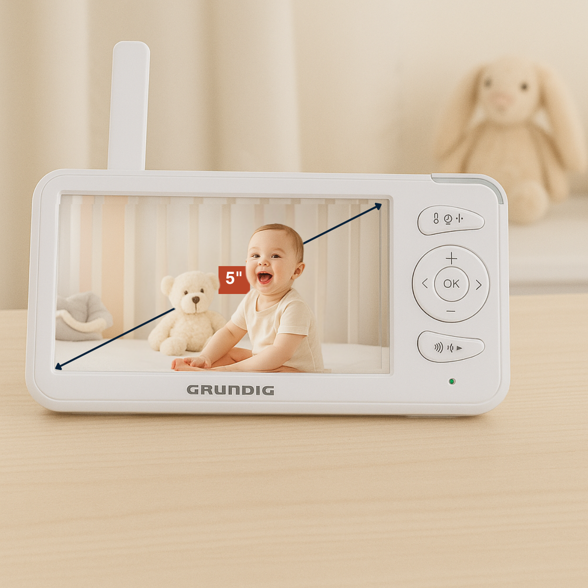 A baby monitor displays a baby and teddy bear. The monitor is on a wooden table. There is a rabbit in the background.