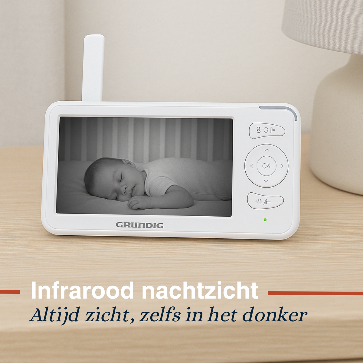 A white baby monitor displays a sleeping infant. The monitor is on a light wood surface.