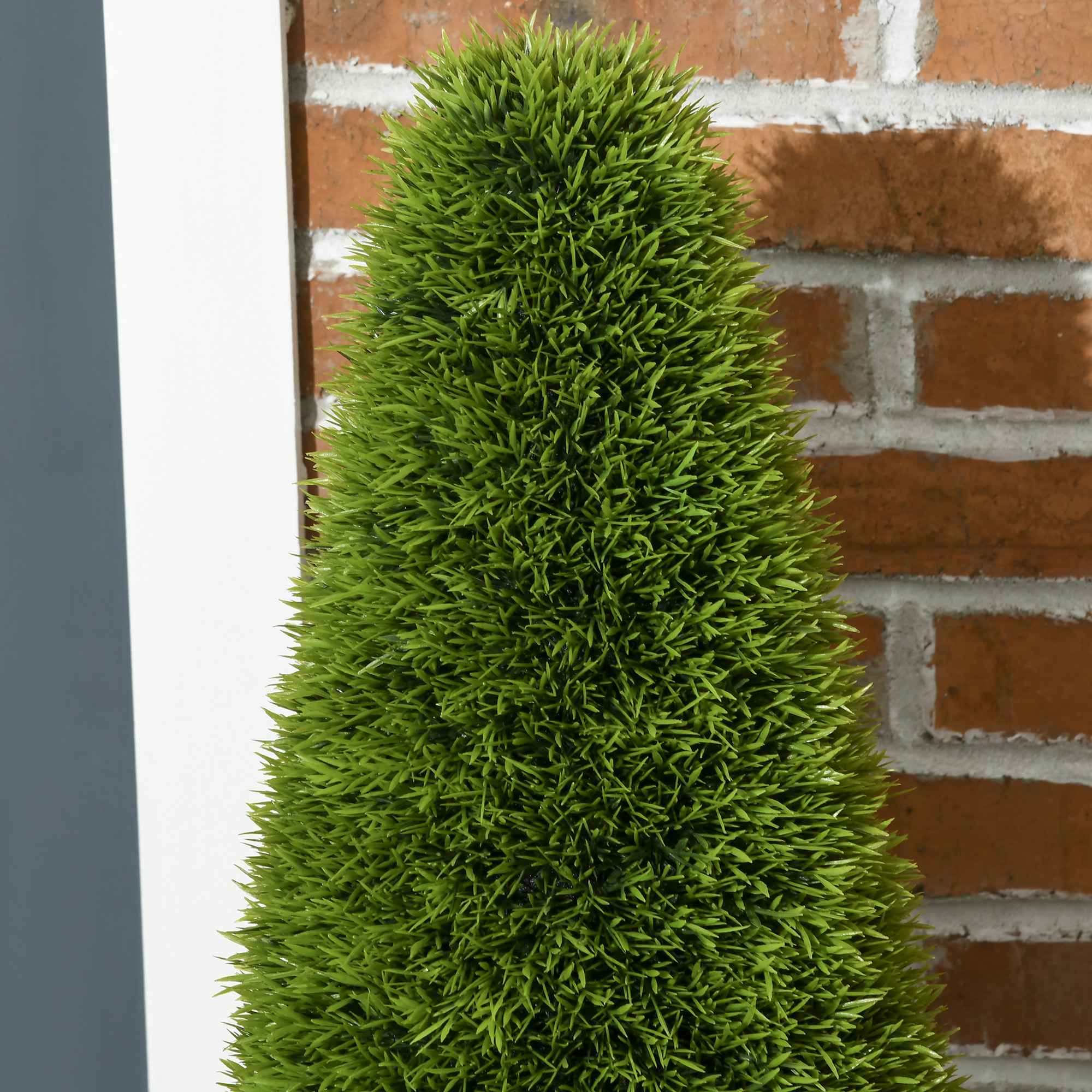 Nahaufnahme eines grünen Topiary-Baums vor einer Backsteinmauer.