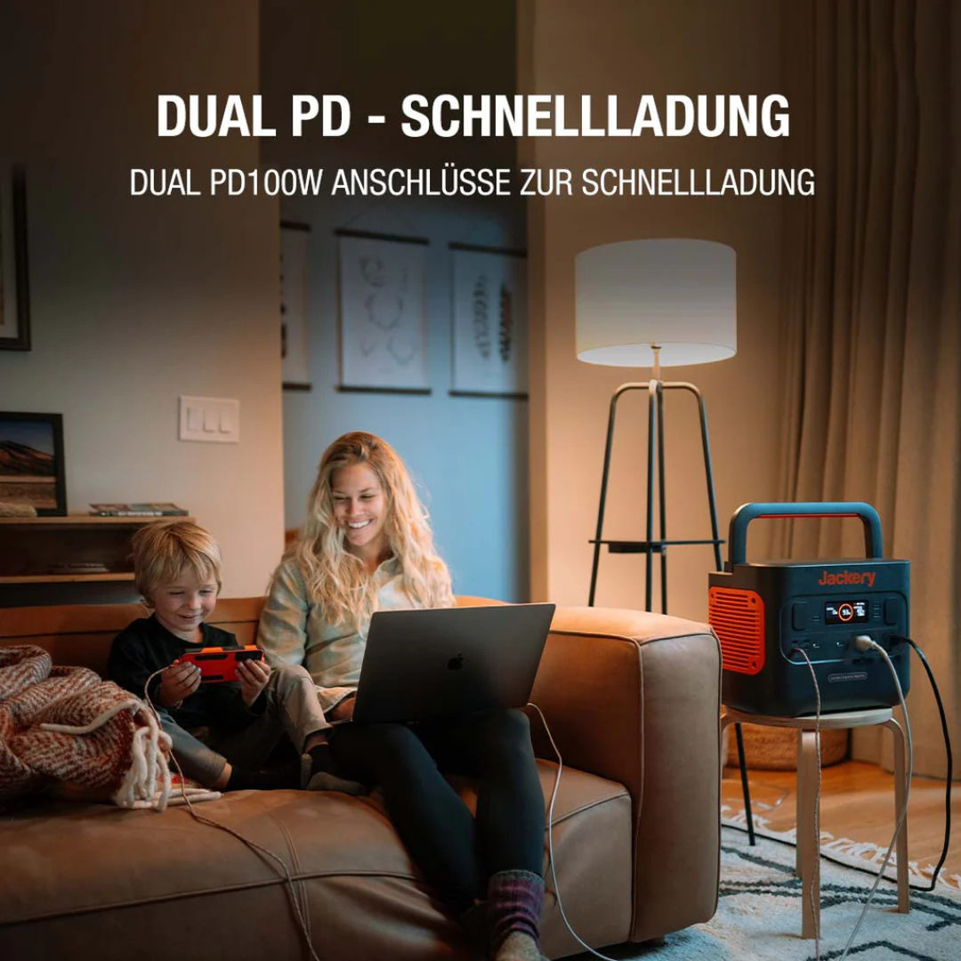 Eine Frau und ein Kind sitzen auf einem Sofa, das Kind spielt ein Spiel, die Frau arbeitet am Laptop. Eine Powerstation ist in der Nähe.