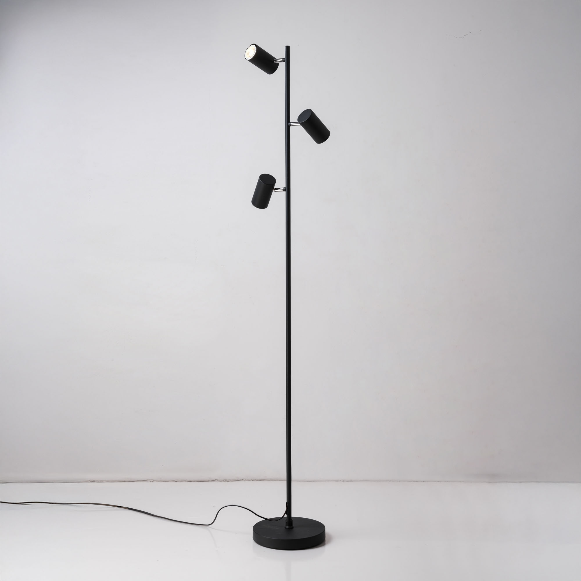 Eine schwarze Stehlampe mit drei Strahlern, vor weißem Hintergrund, mit Kabel.