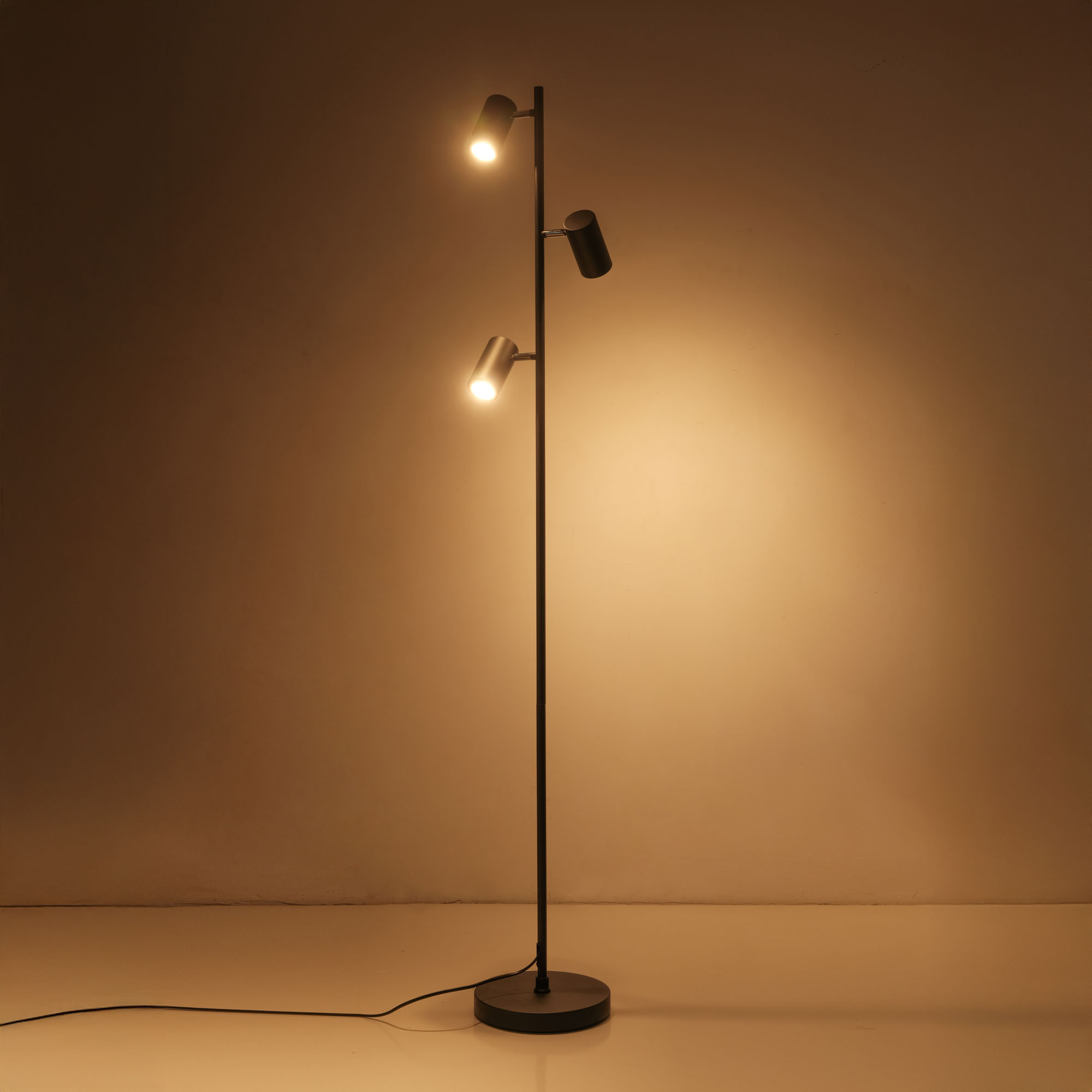 Eine Stehlampe mit drei Strahlern. Zwei sind an, einer ist aus. Der Hintergrund ist braun.